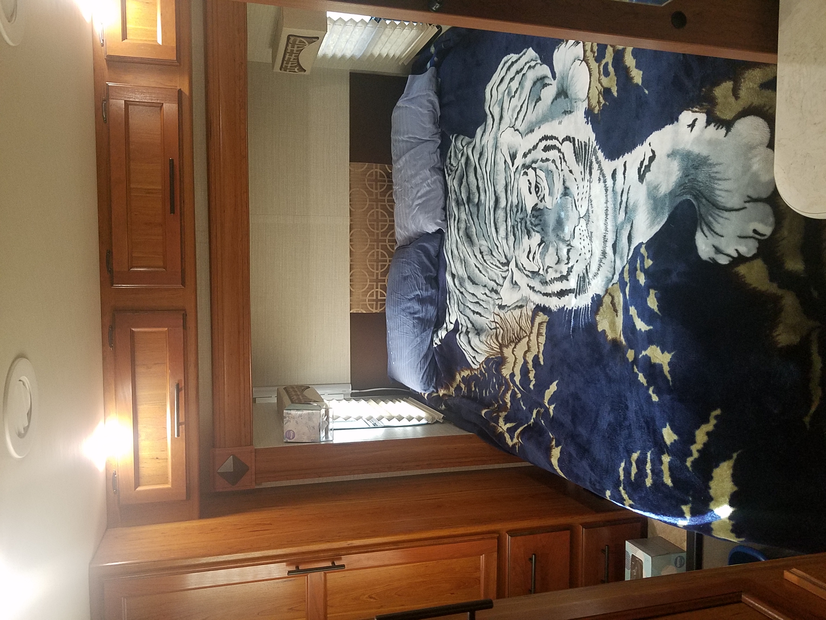 RV rental bedroom: a bed with a striking white tiger blanket, warm wooden cabinetry, and window blinds. Compact & inviting interior.. Jayco Melbourne 2017