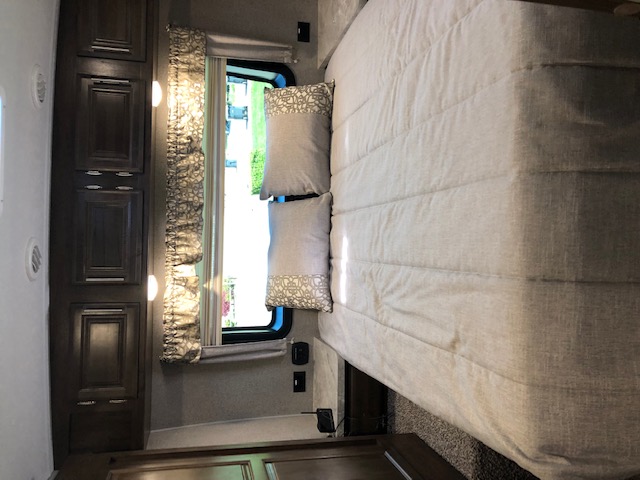 Inside a well-appointed RV rental bedroom: queen bed, dark cabinets, and a sunlit window with patterned curtains.. Forest River Rockwood Ultra Lite 2020