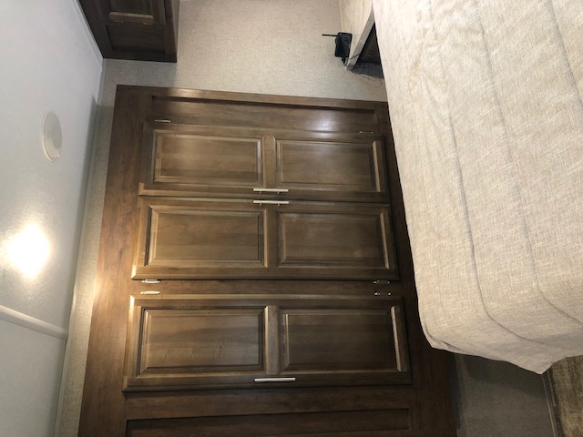 Inside an RV rental: view of a modern bedroom with ample dark wood storage cabinets and a cozy bed, ideal for travel.. Forest River Rockwood Ultra Lite 2020