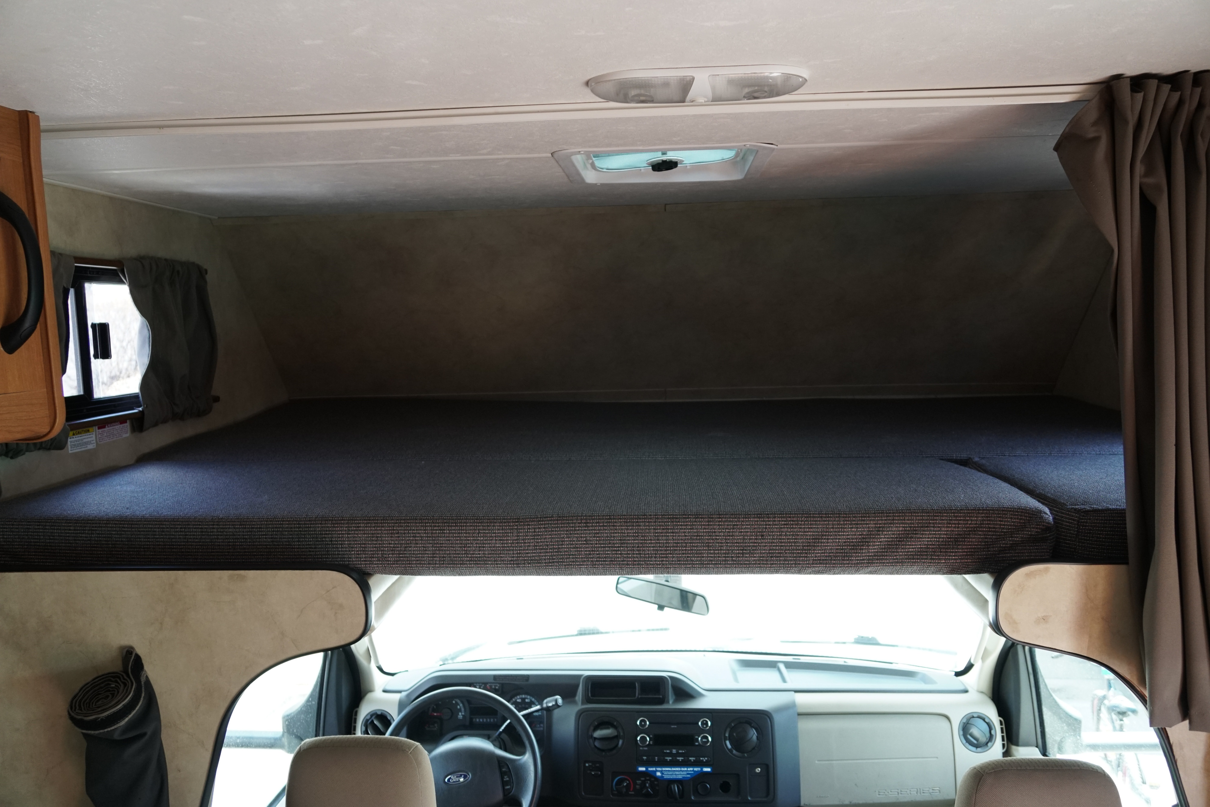 Inside an RV rental, showing the overhead bunk bed and vehicle's front cab below, offering extra sleeping space.. Majestic Leisure Craft 23A 2014