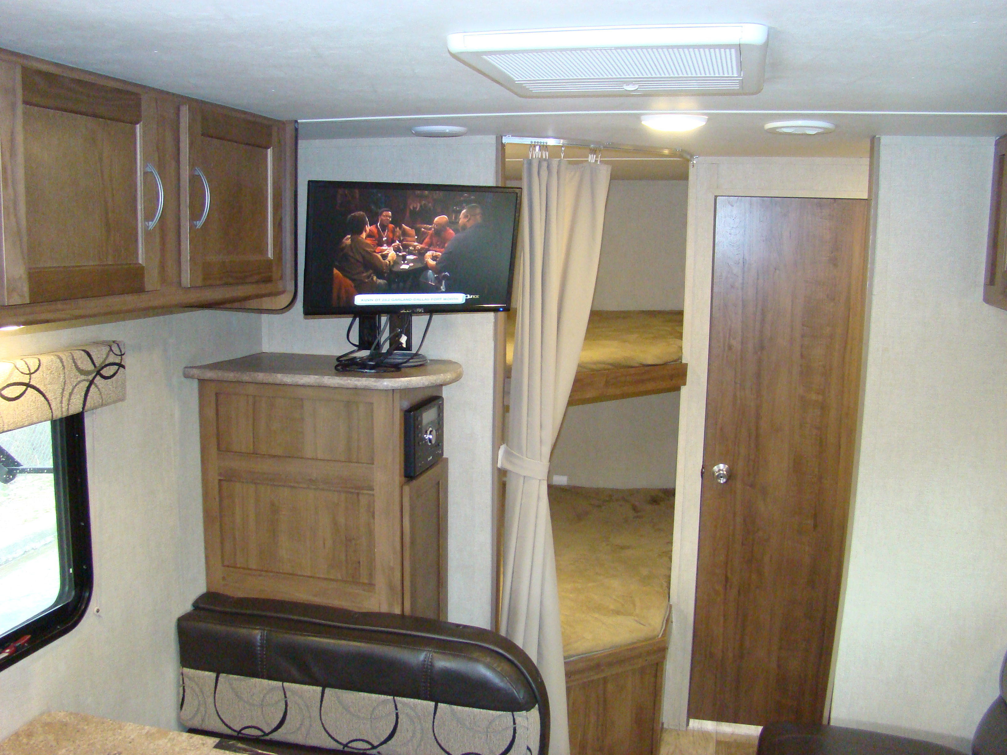 Compact RV rental interior with wooden cabinets, a TV, dinette seating, and cozy bunk beds tucked behind a curtain.. Conquest 275FBG 2020
