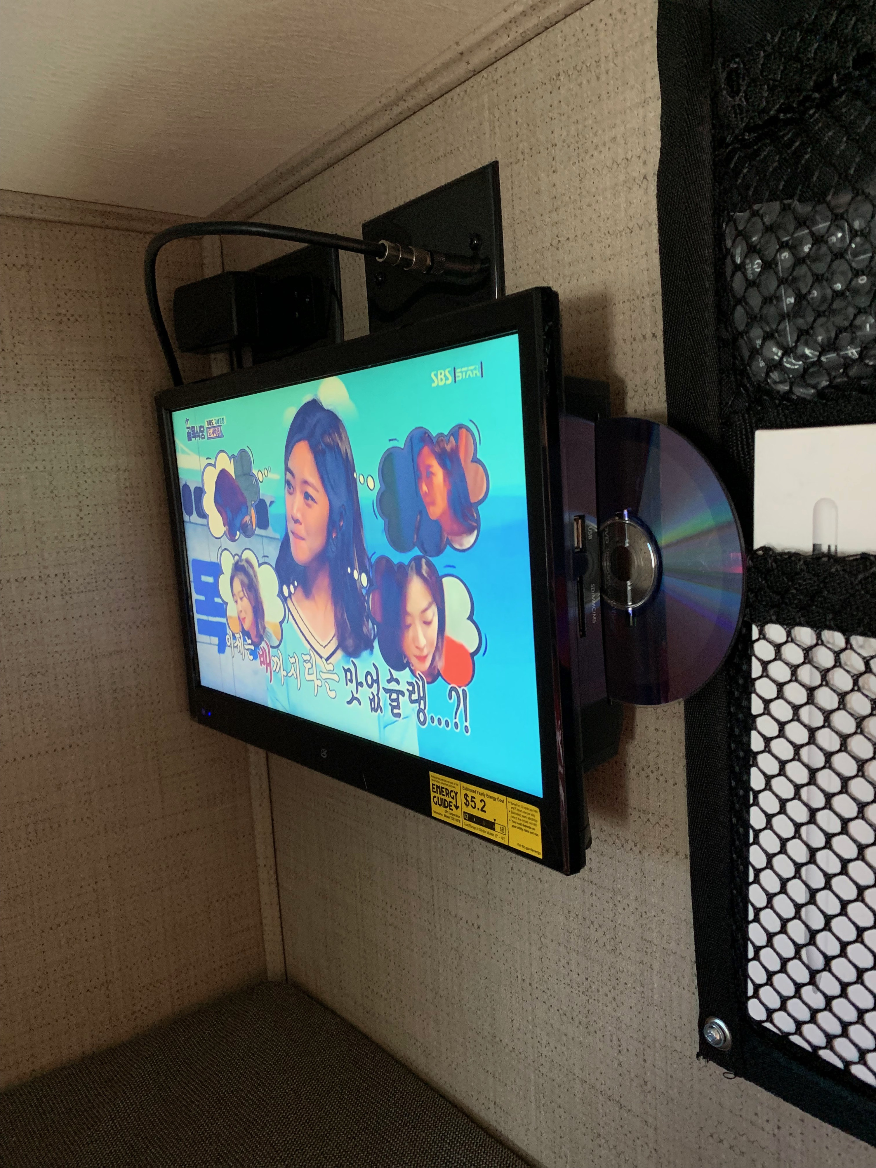 A wall-mounted TV showing a Korean program with a disc partially inserted, typical of an RV rental setup. Energy guide label on screen.. Thor Quantum 2019