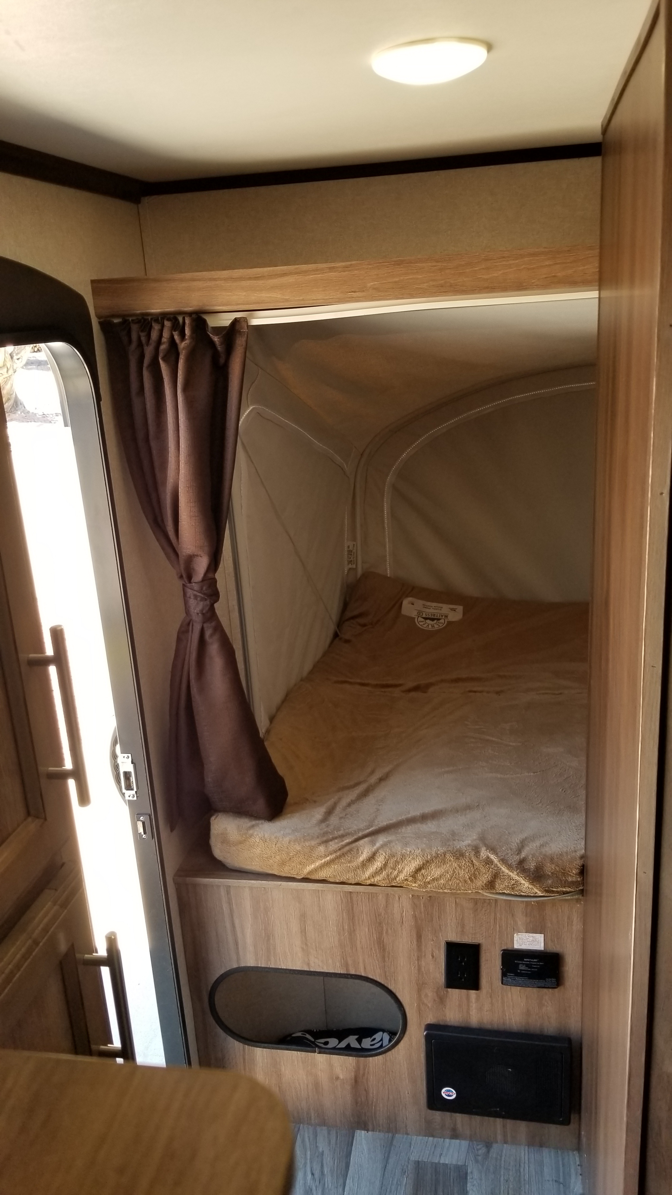 A cozy RV rental interior featuring a pop-out bed, tied-back curtain, and essential power outlets near an open door.. Jayco Jay Feather 2018