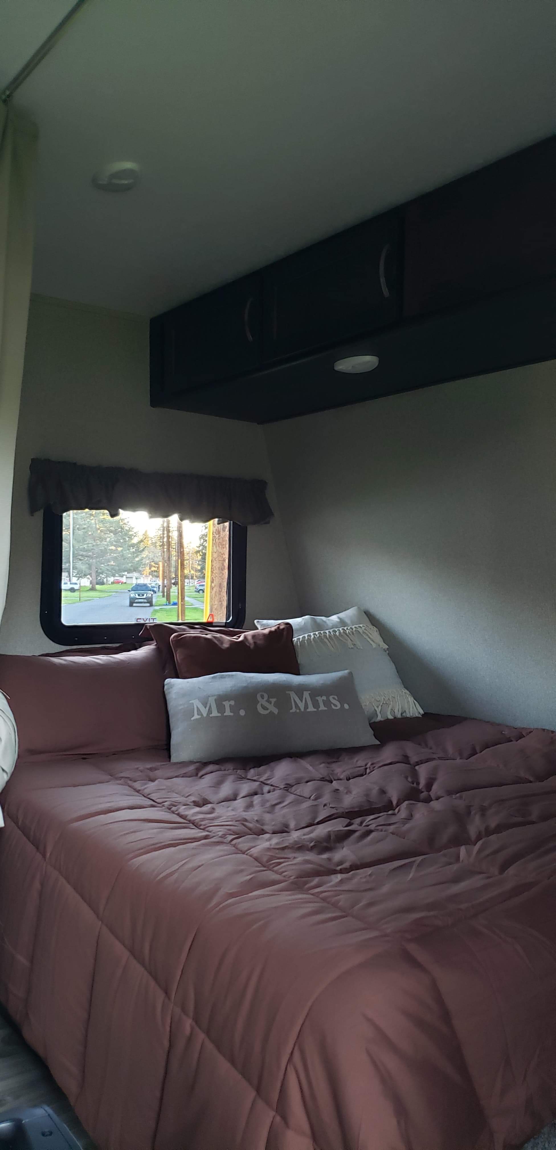 Cozy RV rental bedroom featuring a comfy bed with 'Mr. & Mrs.' pillow, overhead storage, and window view.. Keystone RV Springdale Eco-Lite 2019