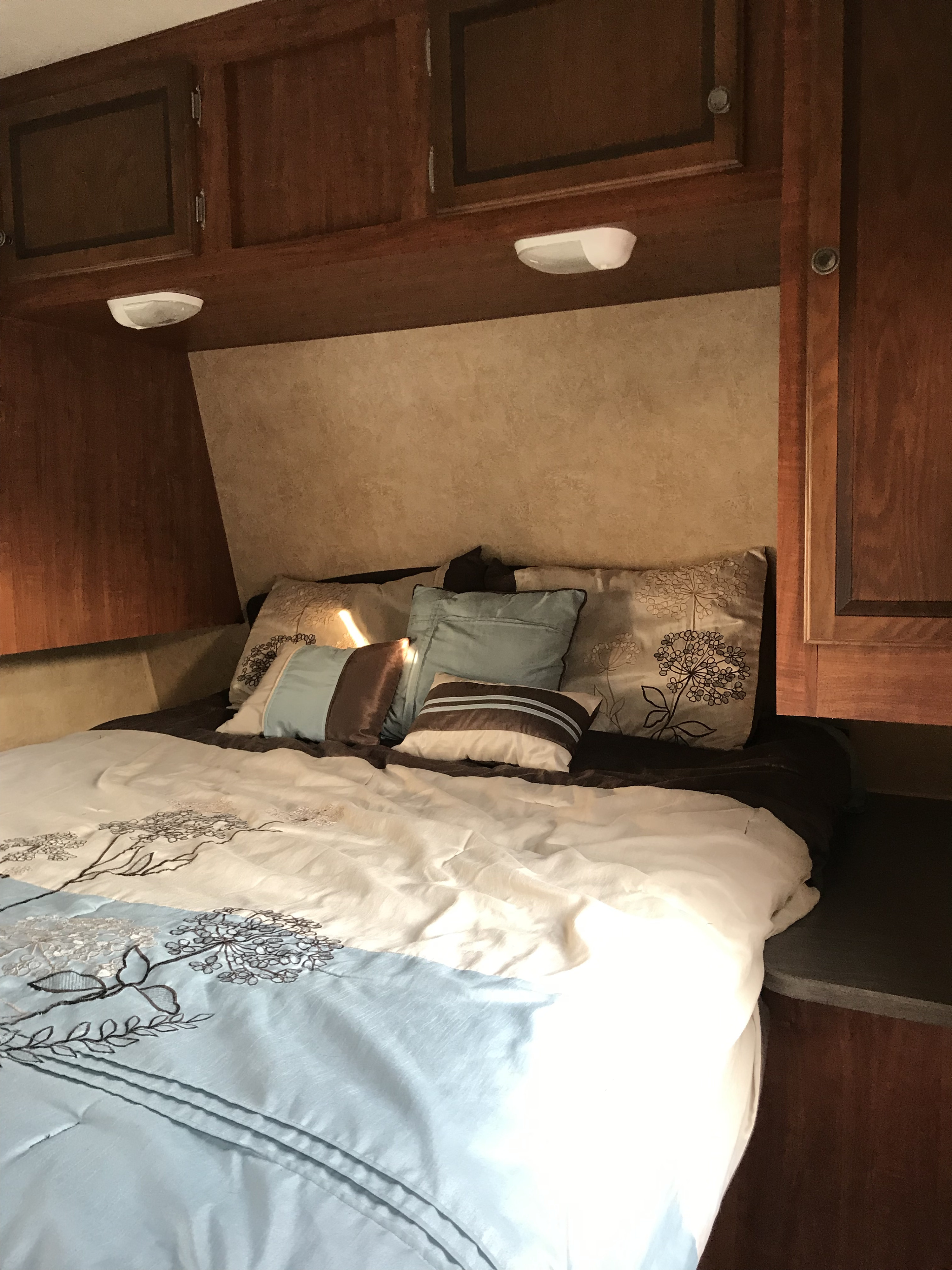 Cozy RV rental bedroom interior featuring a comfortable bed with decorative bedding, pillows, and overhead cabinets.. Jayco Jay Flight 2012