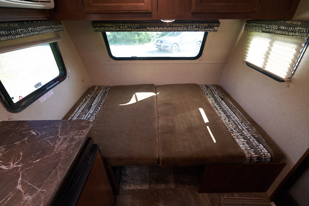 Compact RV rental interior featuring a bed/dinette, multiple windows, and overhead cabinets for storage.. Jayco Baja 154BH 2016