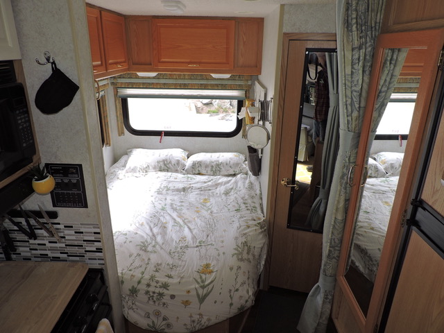 Cozy RV rental interior showcasing a compact bedroom, kitchen area, and full-length mirror.. Itasca Spirit 2002