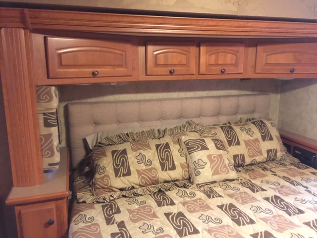 Cozy RV rental bedroom showing a bed with patterned bedding, tufted headboard, and overhead wooden cabinets.. Damon Tuscany 2008