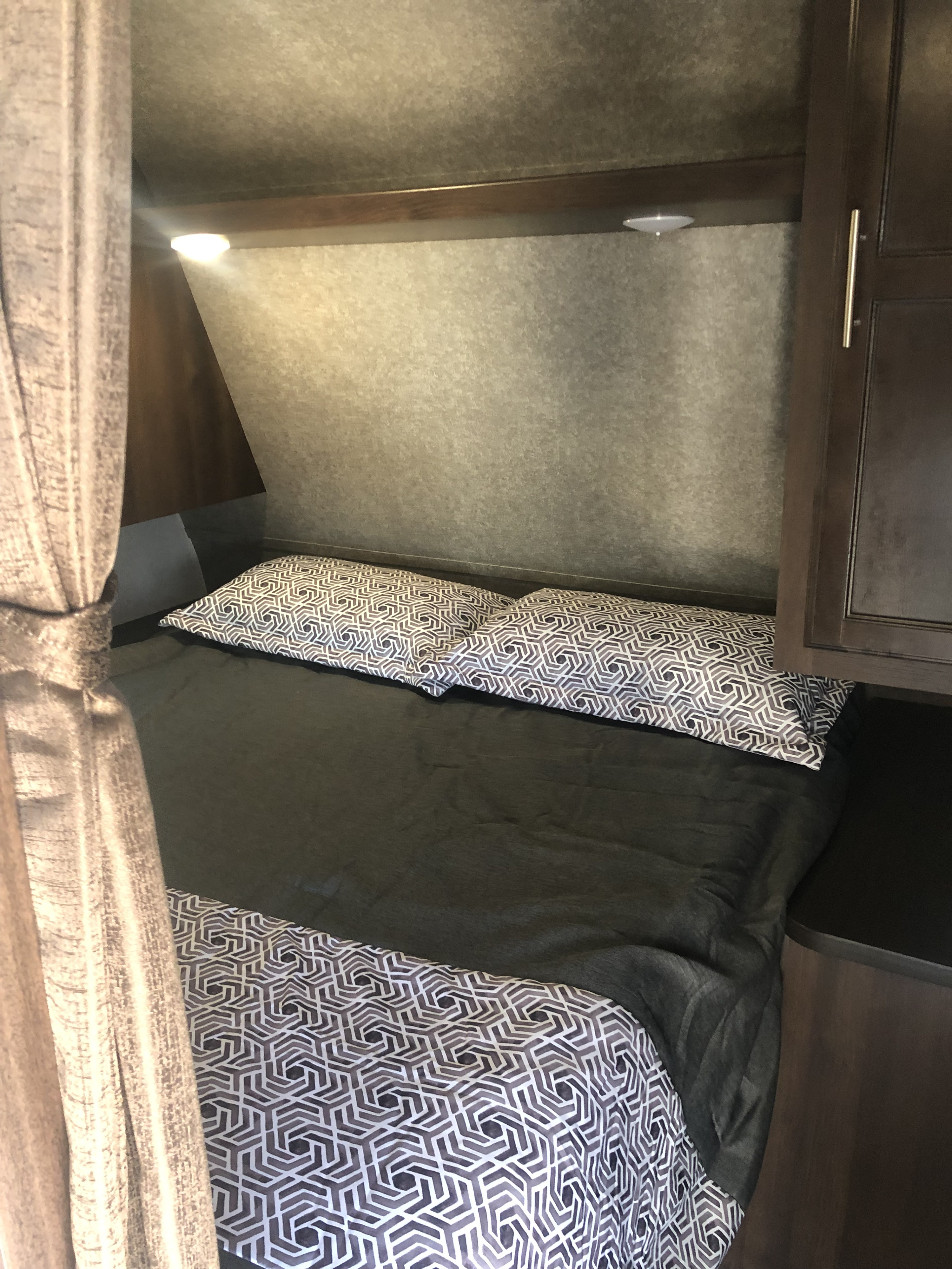 RV rental sleeping area featuring a comfortable bed with modern geometric pillows, dark blankets, and bright reading lights.. Jayco Jay Flight 2019