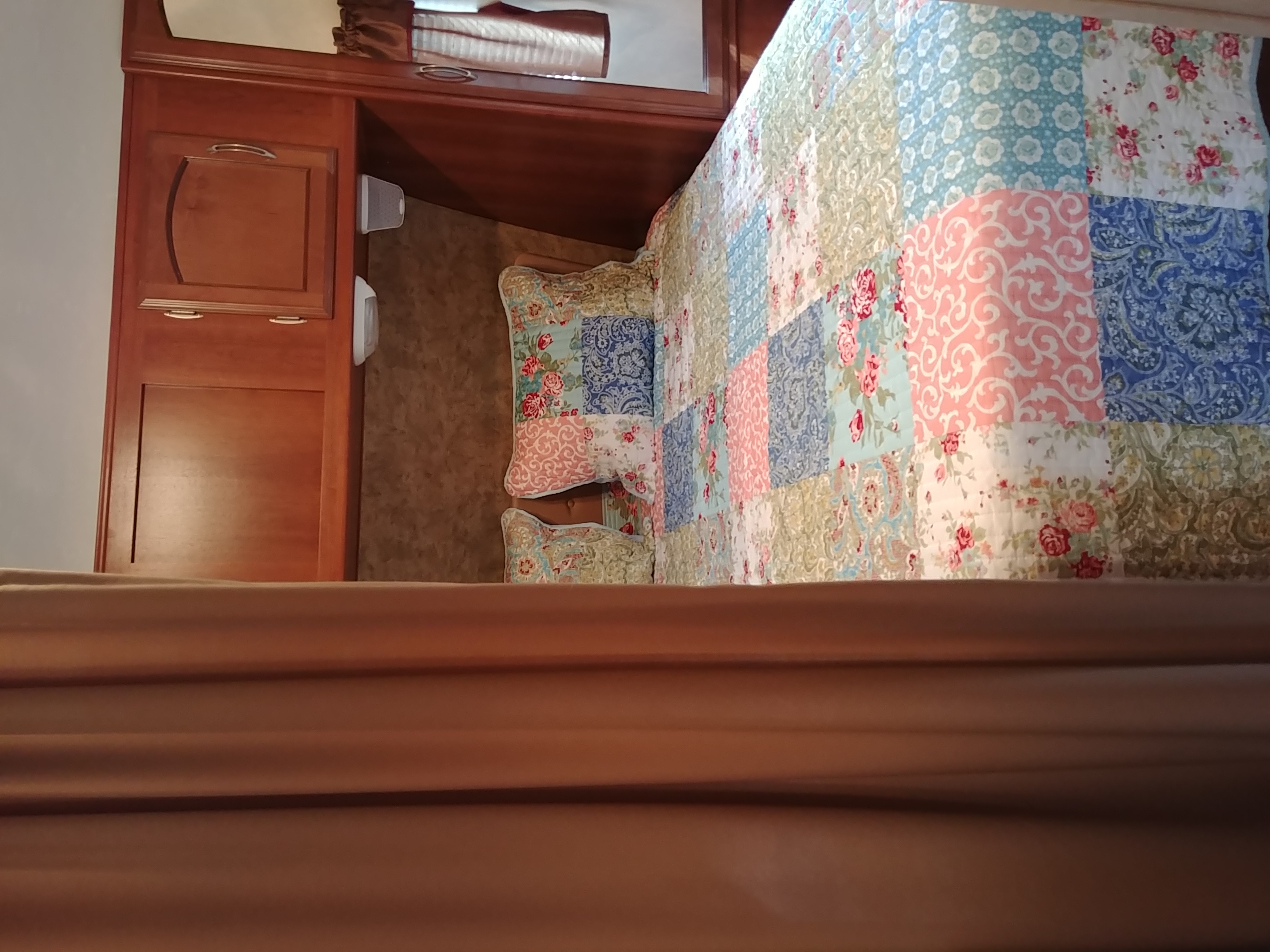 Cozy RV rental bedroom featuring a colorful patchwork quilt, decorative pillows, and built-in wood cabinetry.. Coachmen Freedom Express 2013