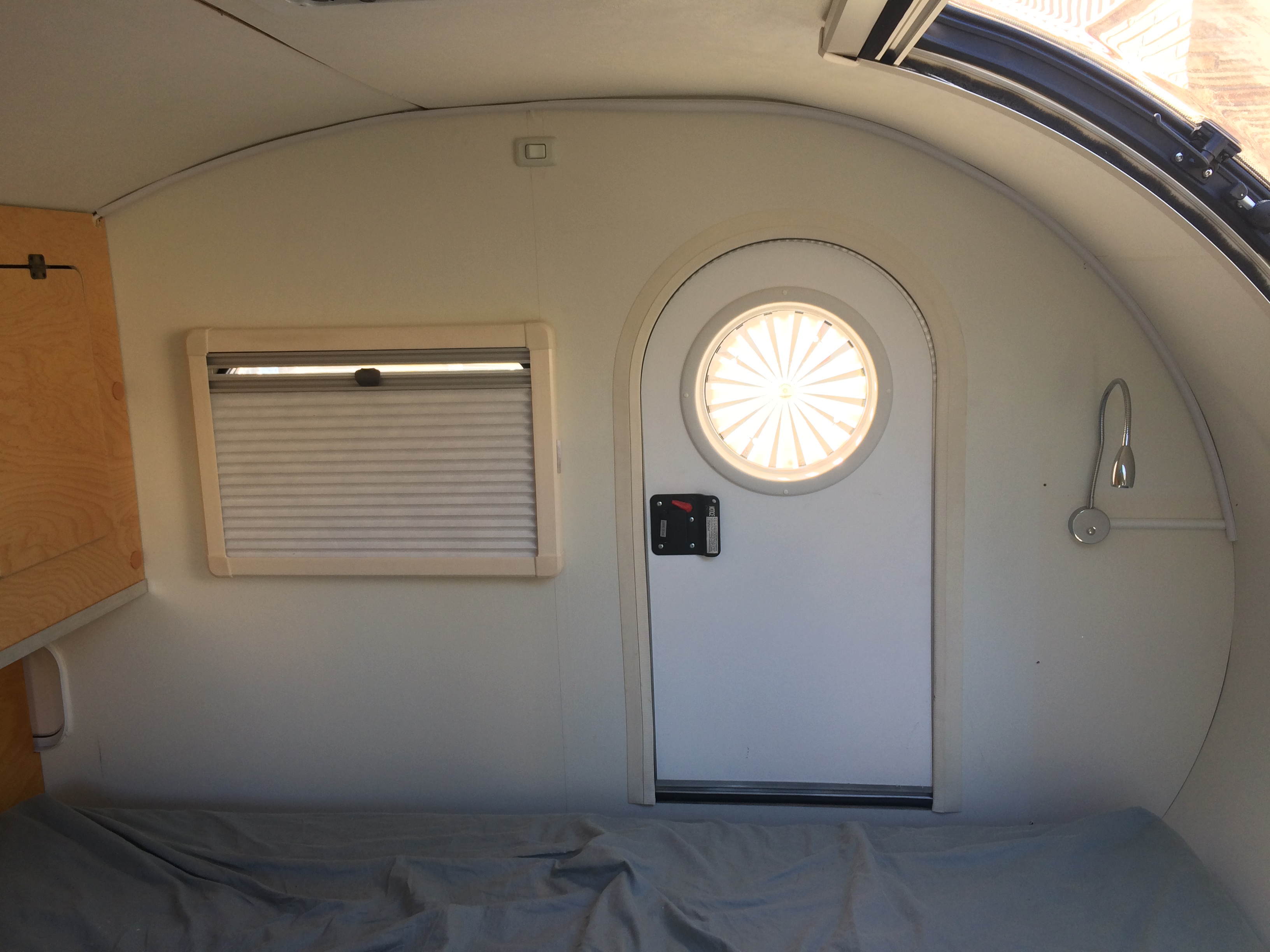 This rv rental interior features a cozy bed, window with blinds, cabinet, and a door with a circular window.. Other Other 2018