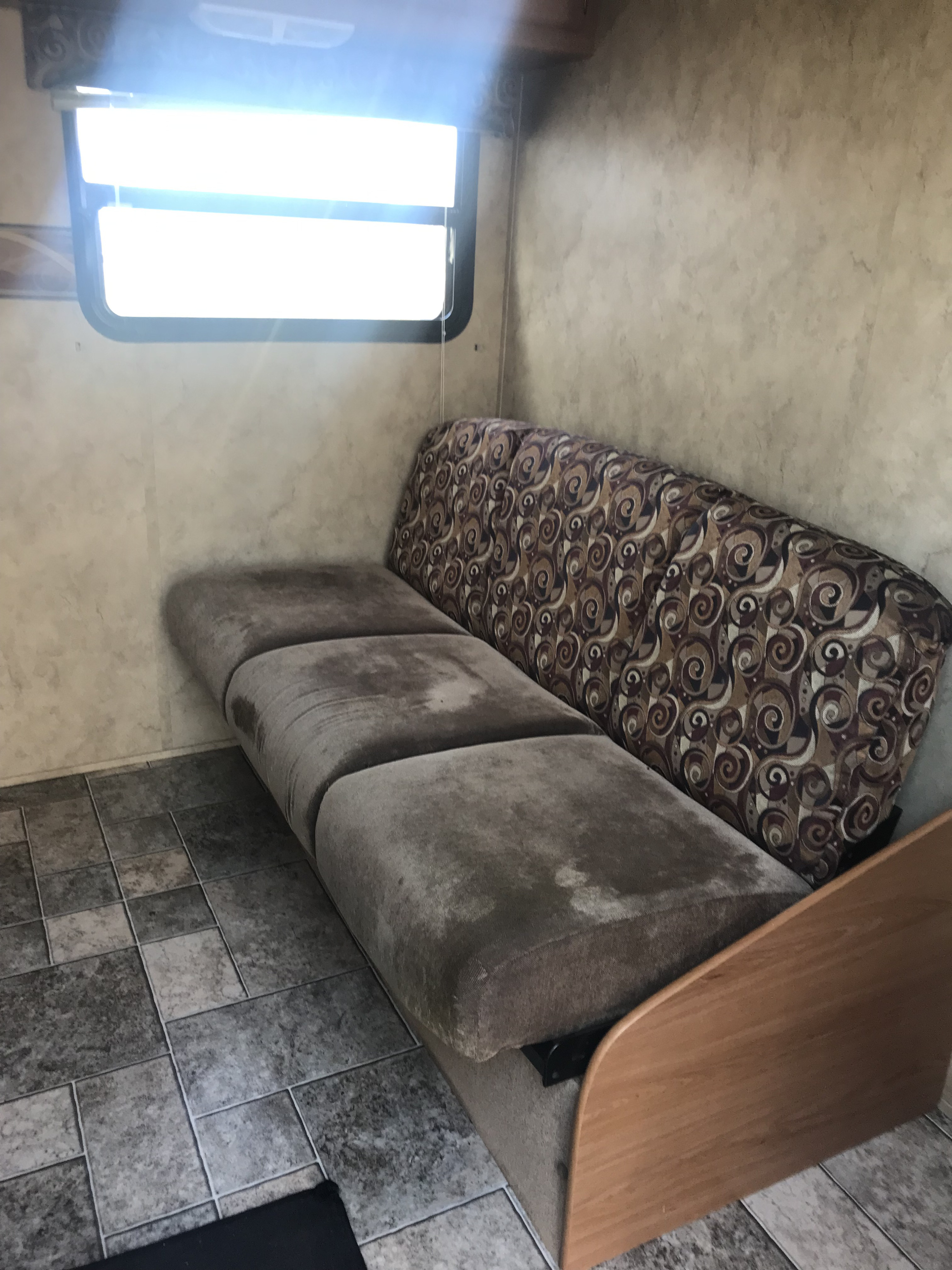 RV rental interior with a well-used sofa, patterned backrest, and bright window. Tiled floor visible.. Keystone Hideout 2009