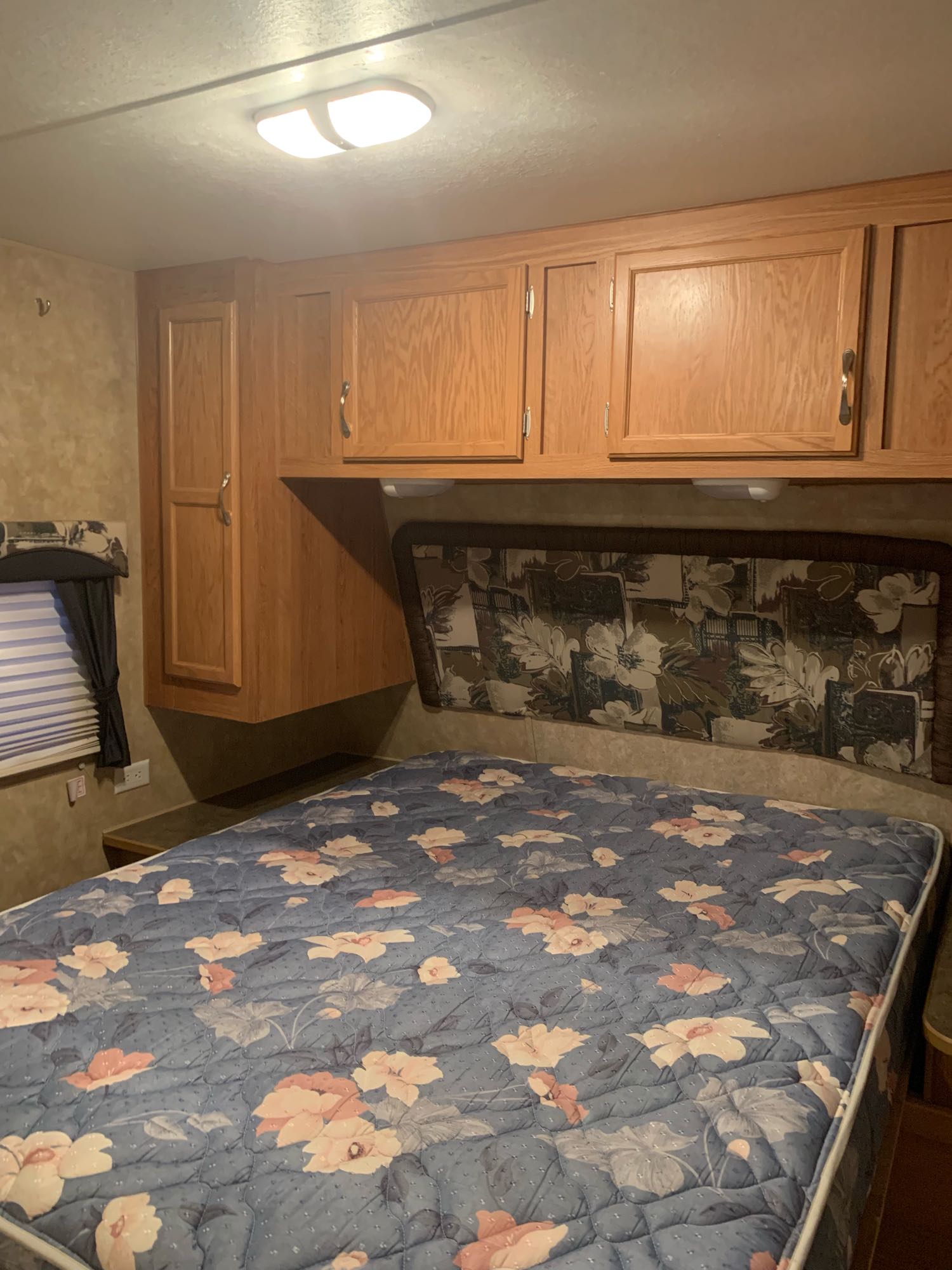 Cozy RV rental bedroom features a floral bed, wooden cabinets, and a window. Perfect for a camper's retreat.. Jayco Jay Flight 2007