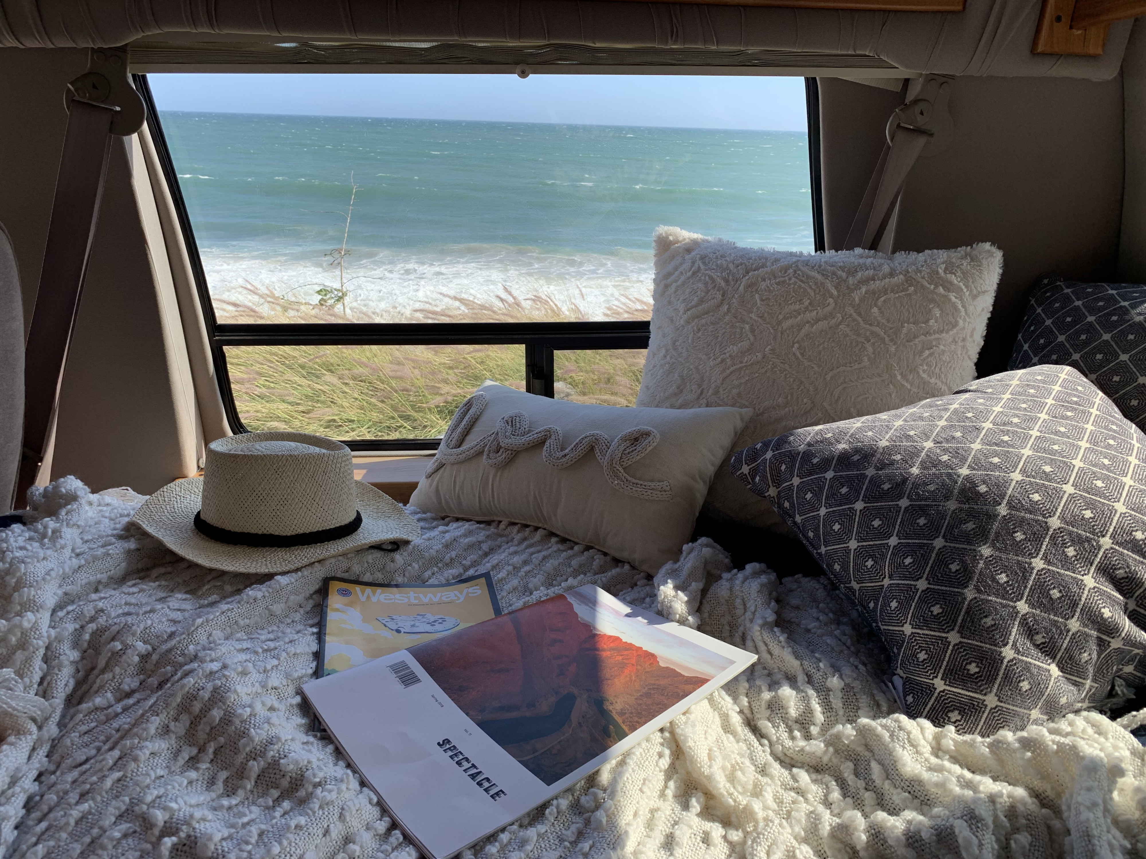 Relaxing RV rental interior with a stunning ocean view, soft pillows, & blanket. Ideal for cozy van travel.. Ford Econoline 150 2004