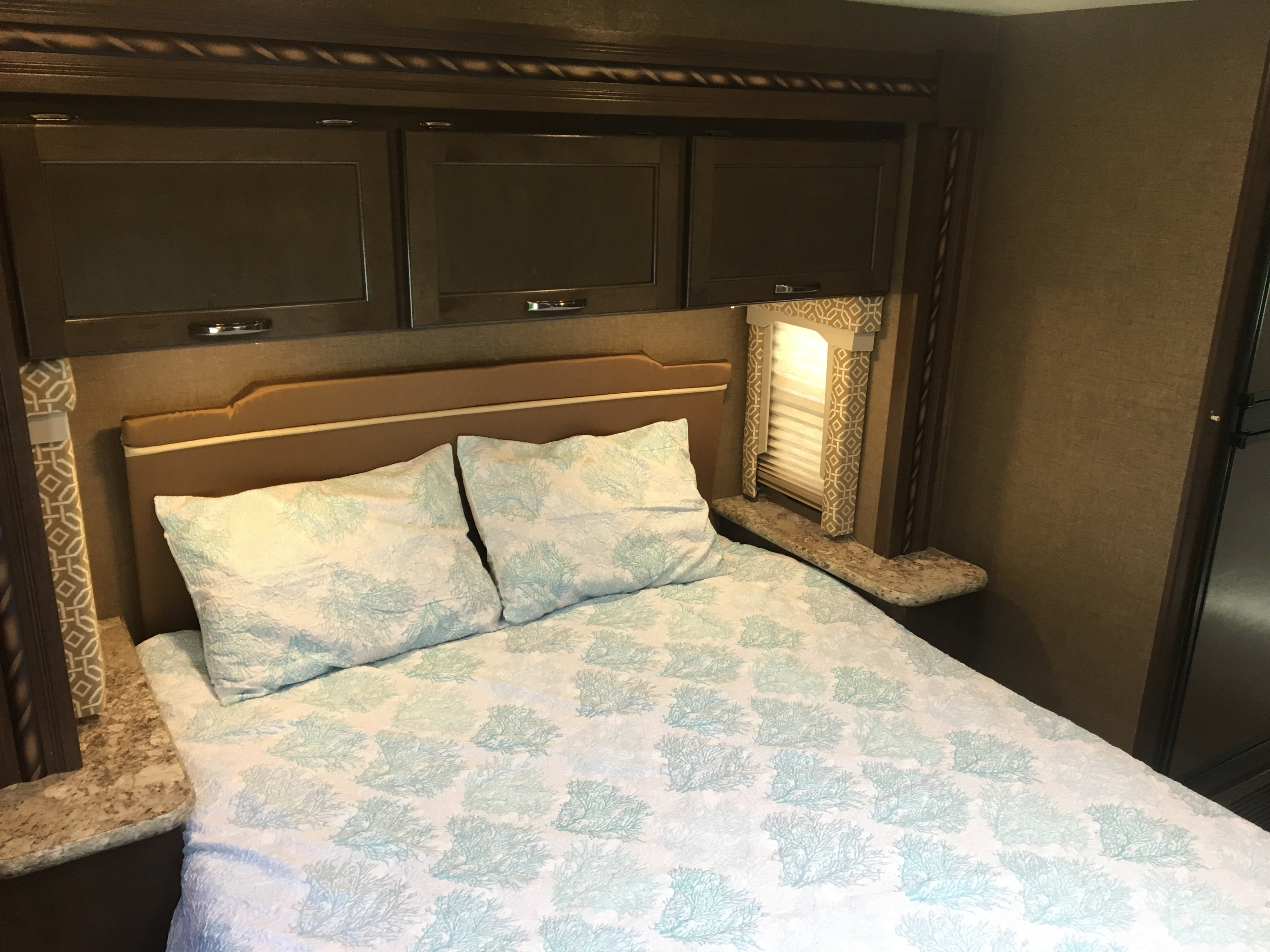 Cozy RV rental bedroom featuring a bed with aqua coral bedding, a brown headboard, and dark wood overhead cabinets.. Thor Freedom Elite 2017