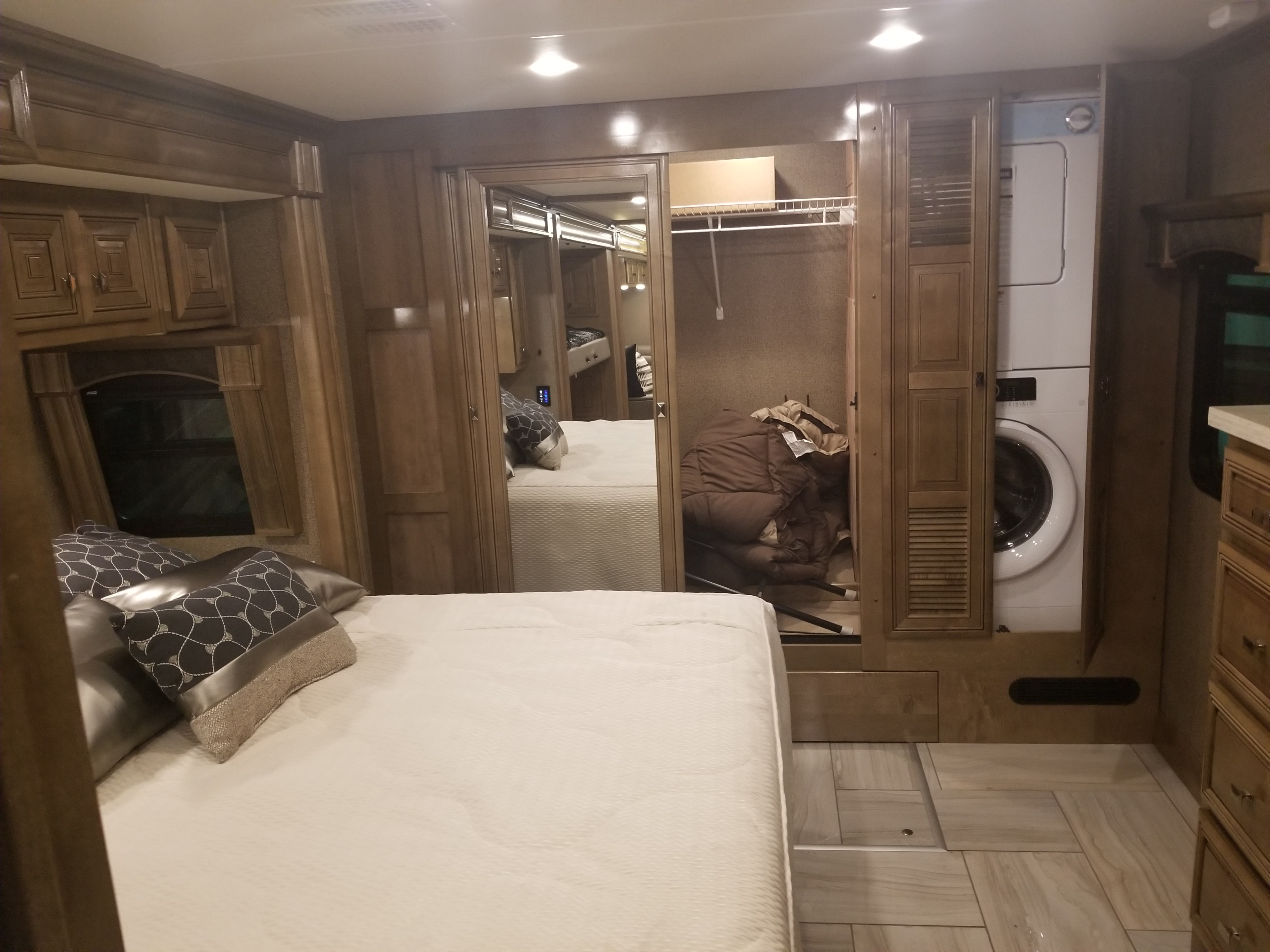 RV rental bedroom with bed, mirrored closet, and stacked washer/dryer. Features wood cabinetry, window, and tiled floor.. Fleetwood Discovery 2019