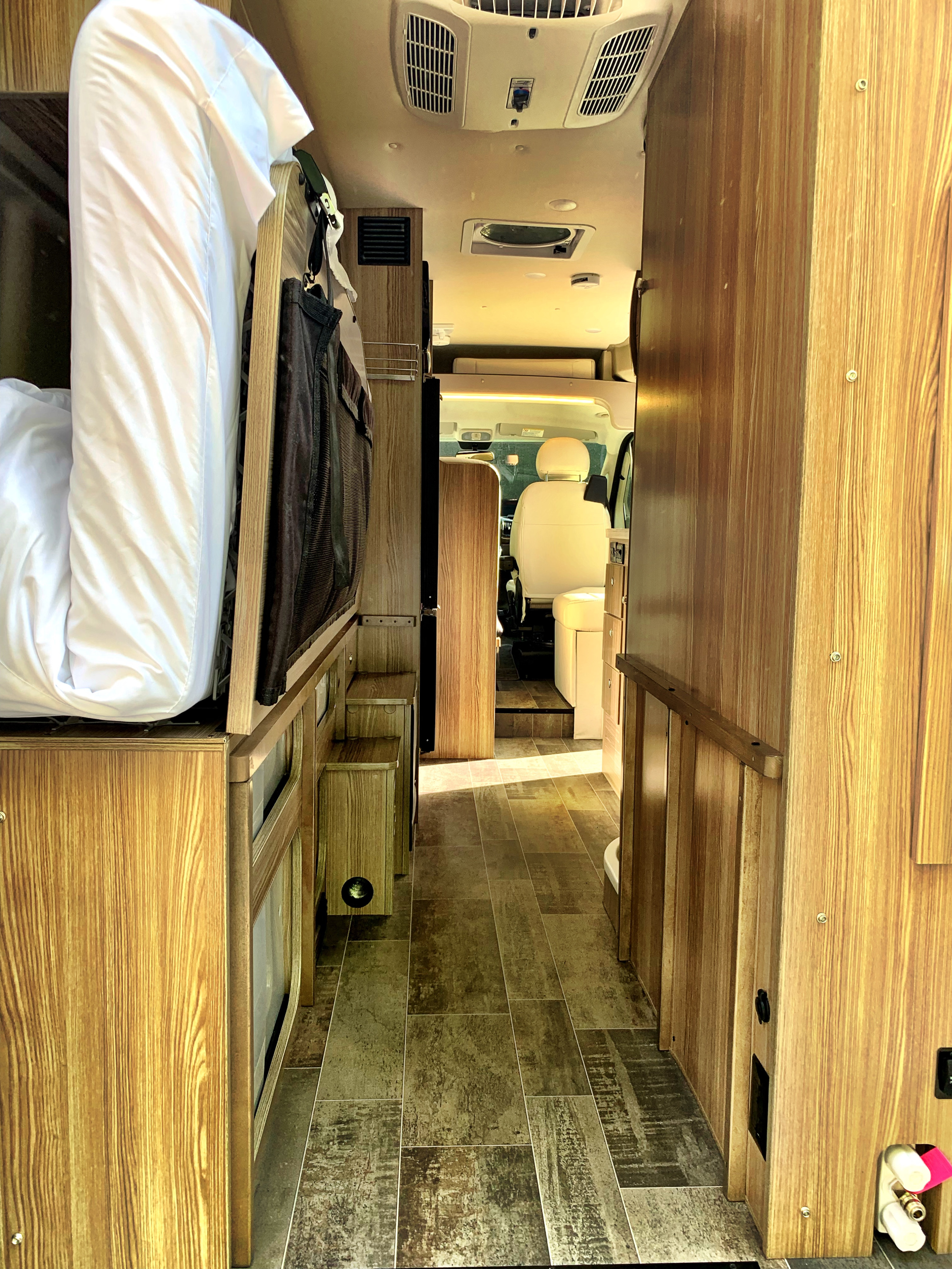 RV rental interior looking forward: bed on left, cabinetry on right, leading to the driver's cabin.. Winnebago Travato 2019