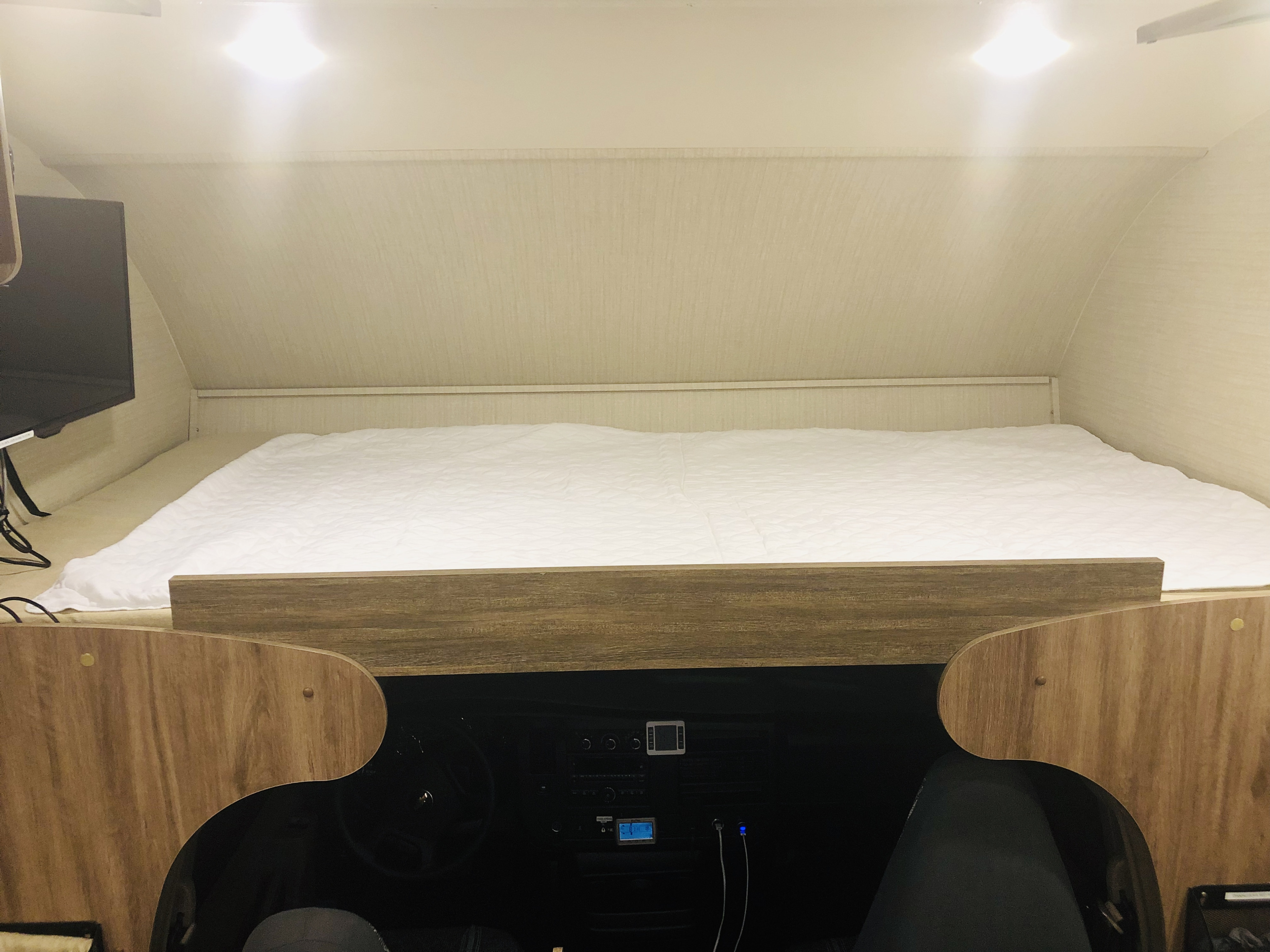 Cozy rv rental interior: A comfortable over-cab bed is situated above the driver's cabin, with a TV to the left.. Jayco Redhawk 2019