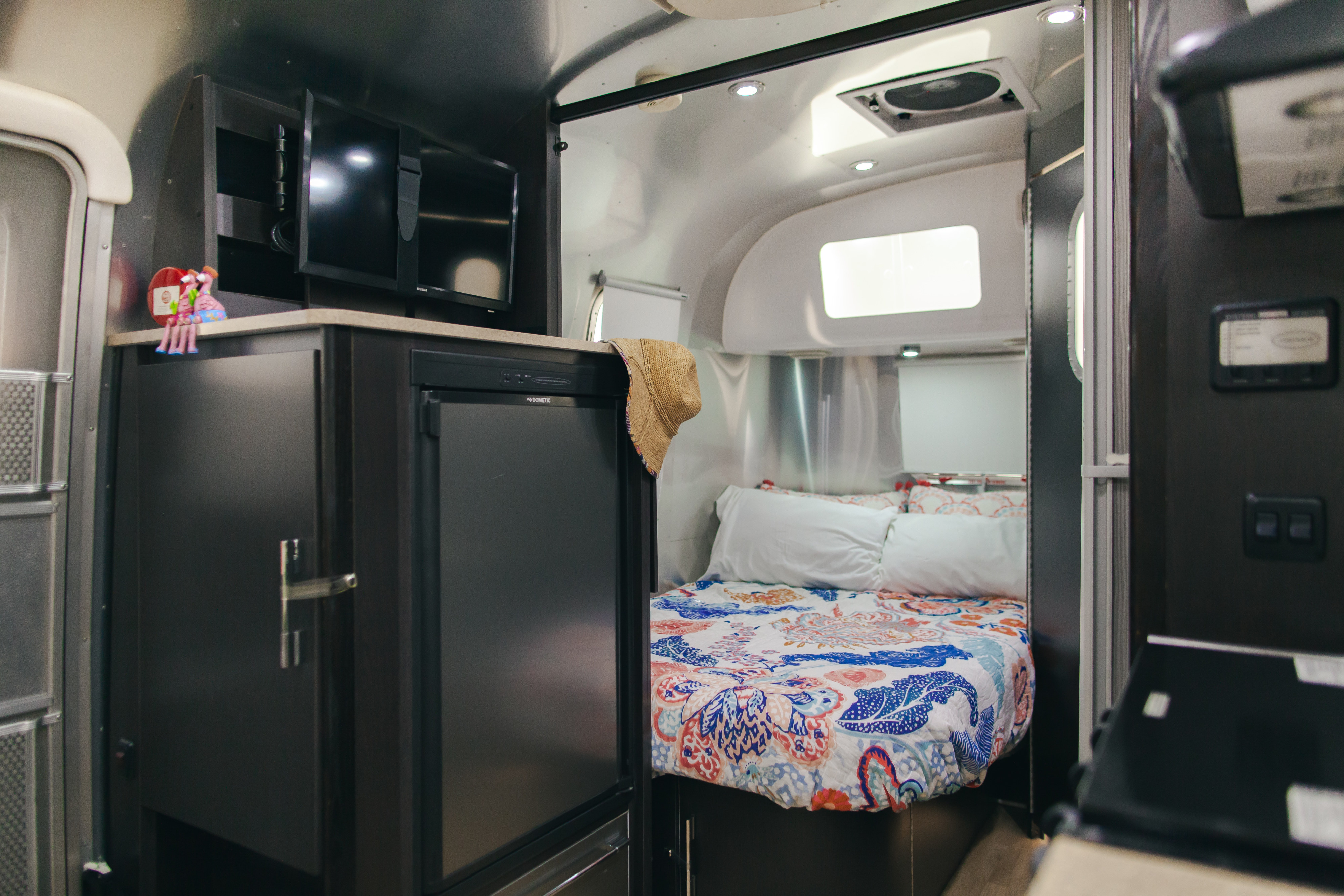 Cozy RV rental interior featuring a comfy bed with colorful bedding, entertainment TVs, and a compact kitchen.. Airstream 19 Bambi International 2012
