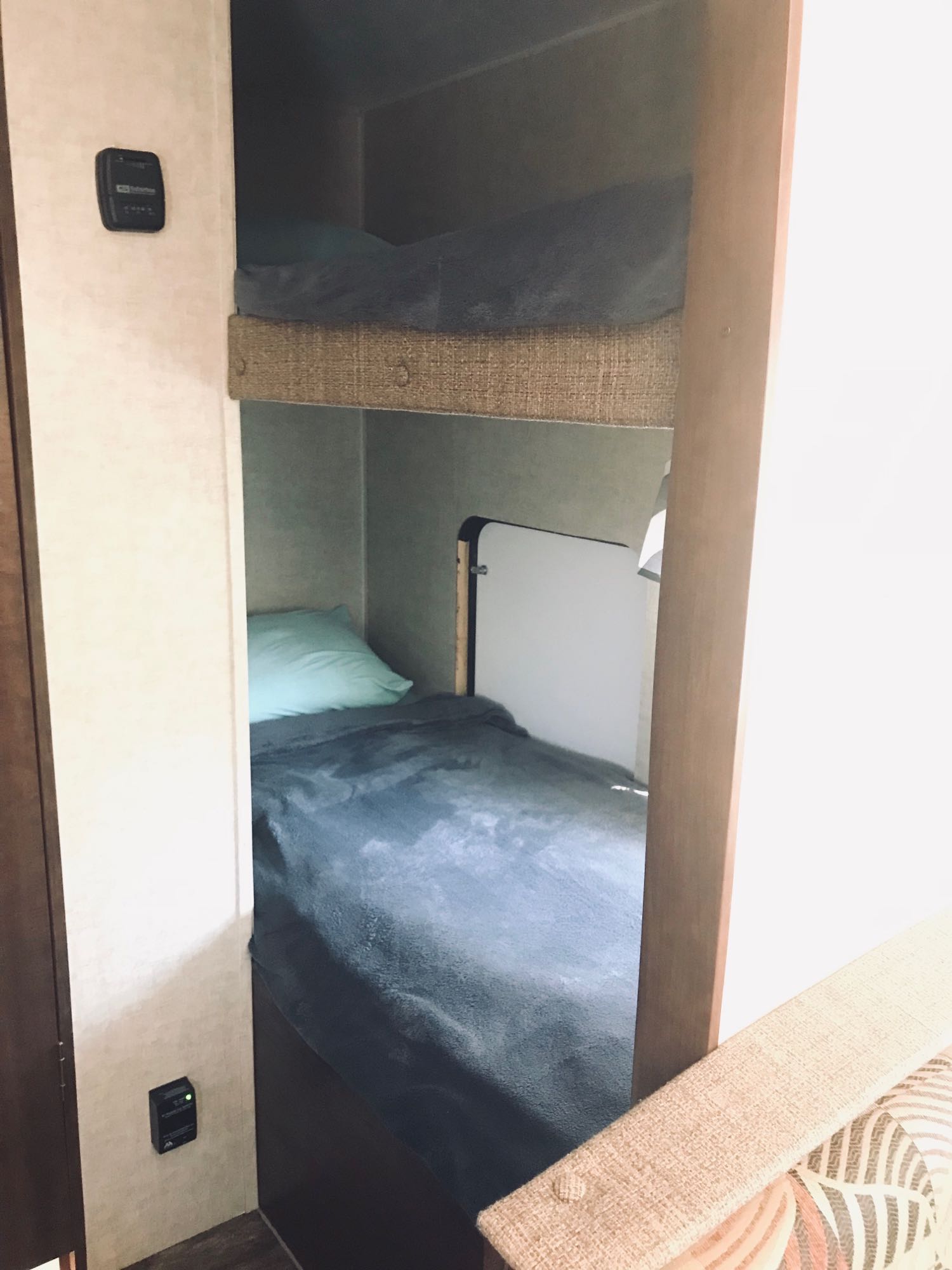 Inside a comfortable RV rental, showing bunk beds ready for use and a wall-mounted control panel.. Keystone Hideout 2016
