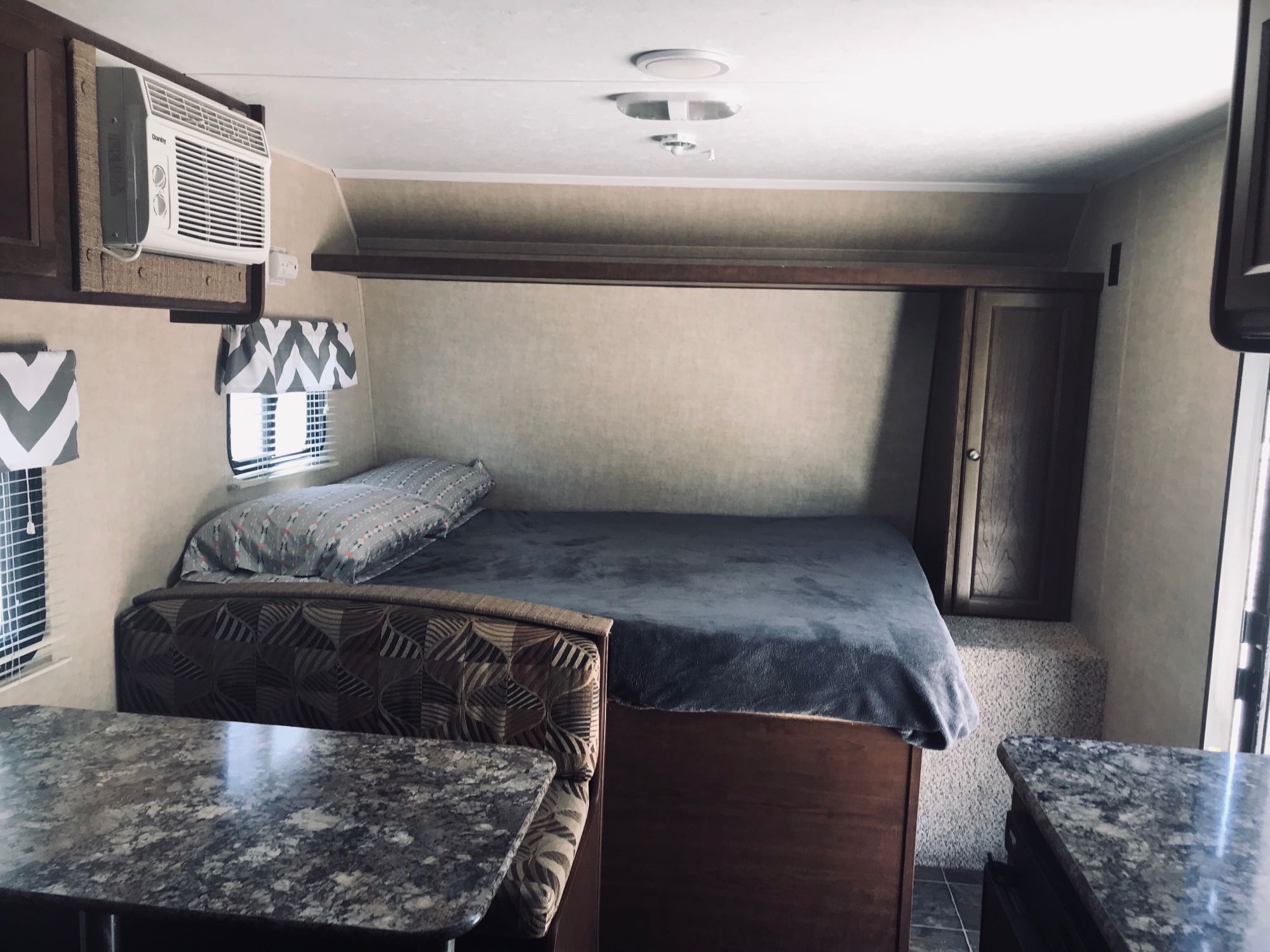 Inside an RV rental: a compact bedroom with bed, an AC unit, and a small dinette area, showing efficient use of space.. Keystone Hideout 2016
