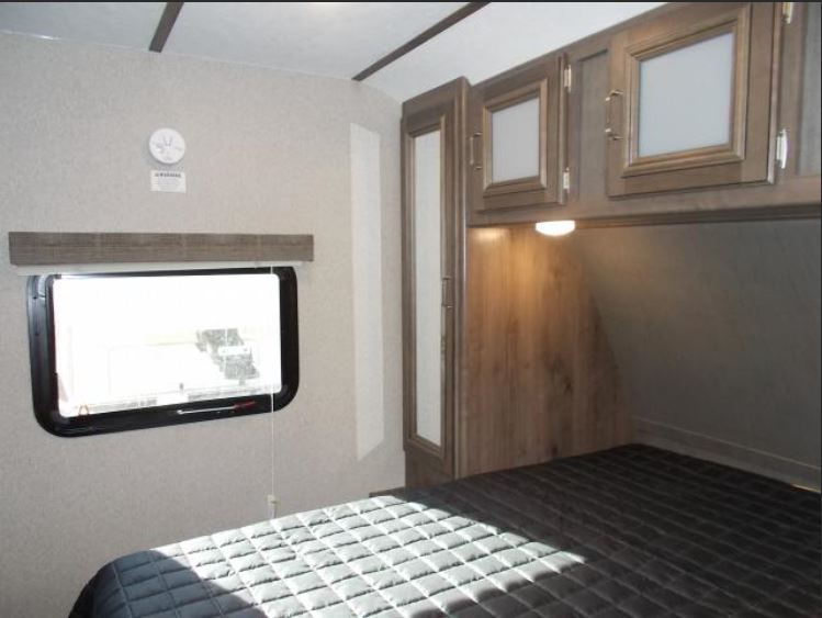 Cozy RV rental bedroom with quilted bed, window, and overhead storage. Ideal for comfortable travel.. Keystone RV Passport Grand Touring 2018