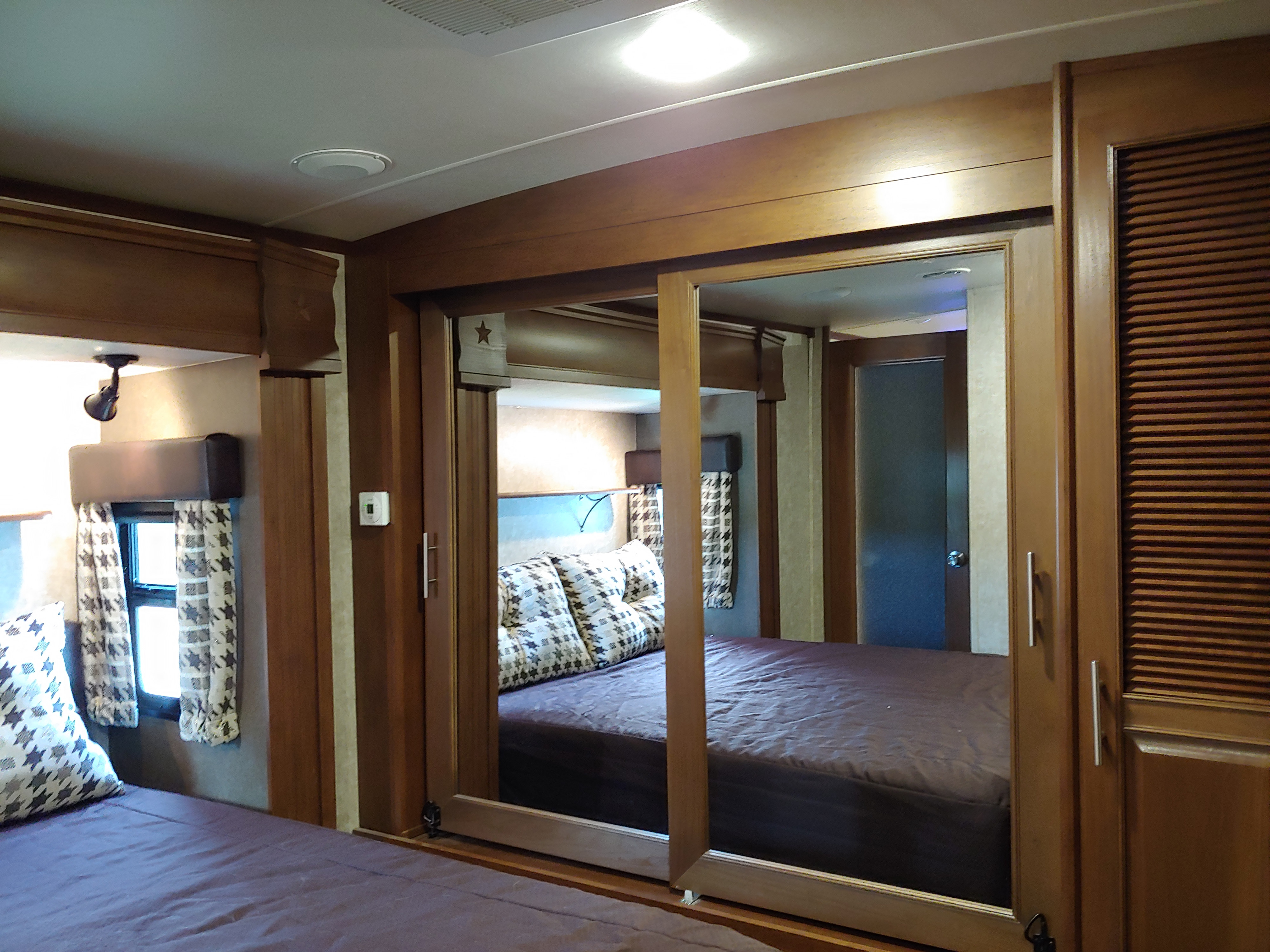 Inside an RV rental, two beds with star pillows and dark bedding are seen, separated by mirrored sliding wood doors.. Open Range 38RGR 2016
