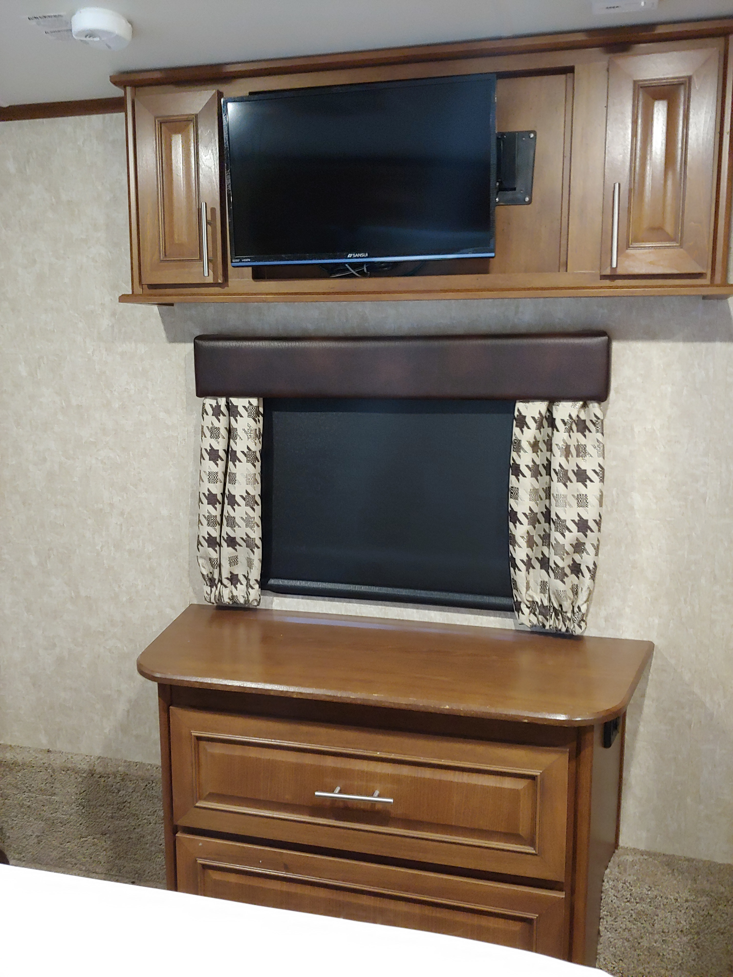 RV rental bedroom showing a mounted TV, window with brown/white patterned curtains, and a wooden dresser.. Open Range 38RGR 2016