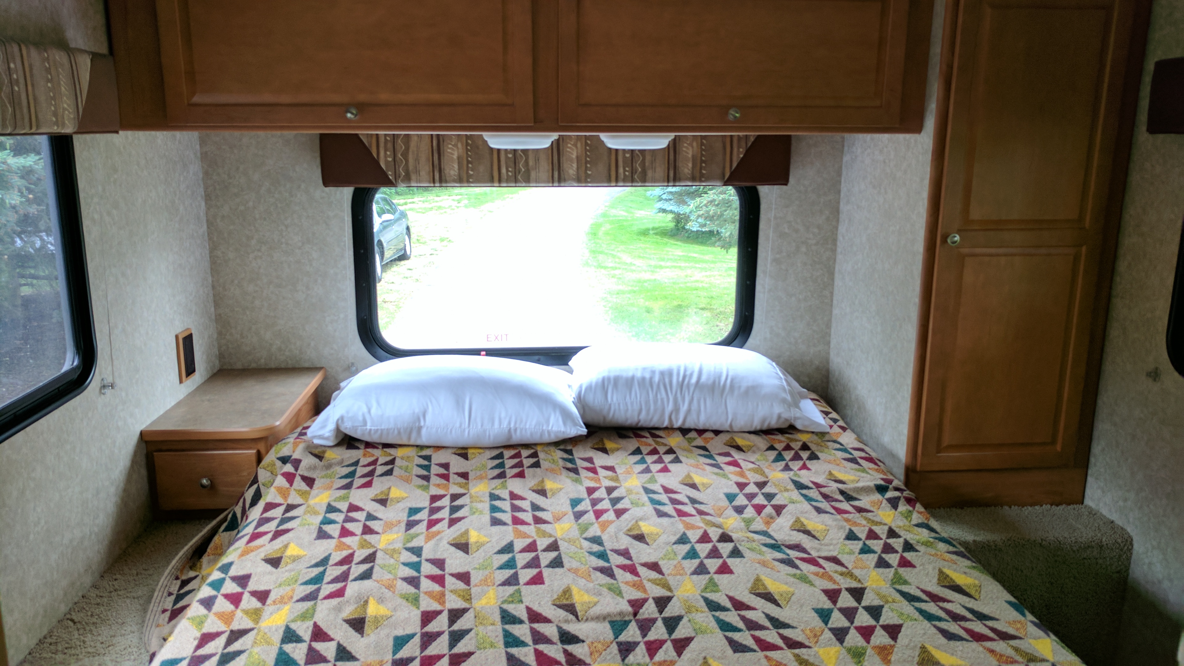 Compact RV rental bedroom with a colorful quilt, white pillows, windows, and wood cabinets for cozy lodging.. Winnebago ITASCA 2009
