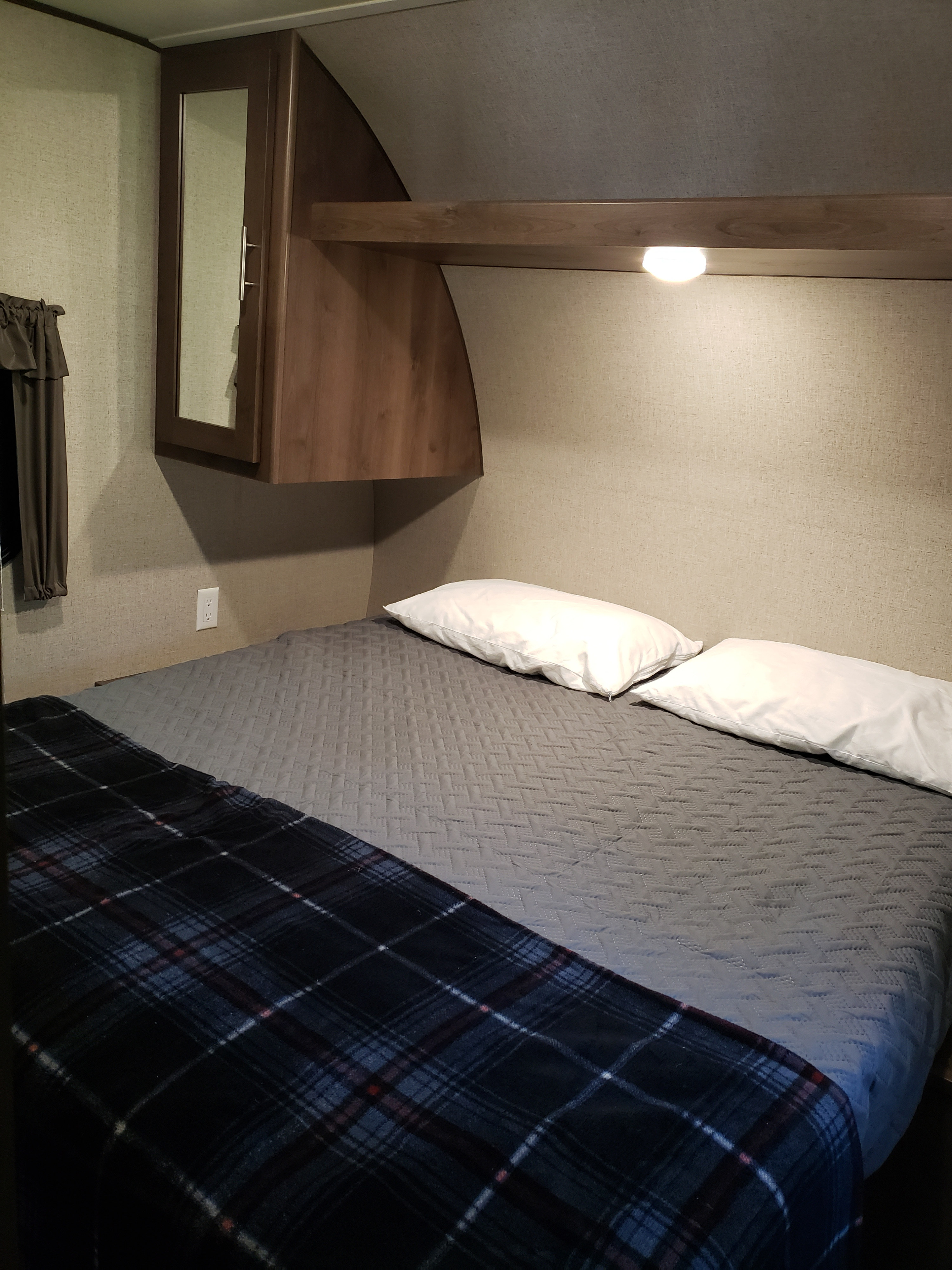Cozy RV rental bedroom featuring a neatly made bed with white pillows, gray quilted comforter, and a plaid blanket.. Shasta Oasis 2019