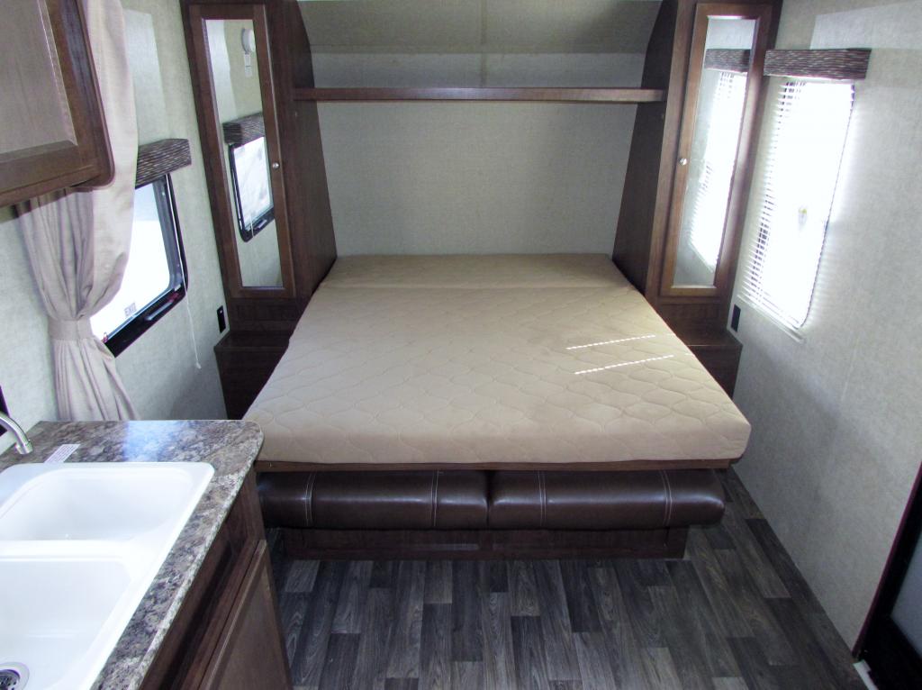 RV rental interior: A cozy convertible bed/sofa with side cabinets, a shelf above, and a kitchen sink on the left.. Keystone Hideout 2017