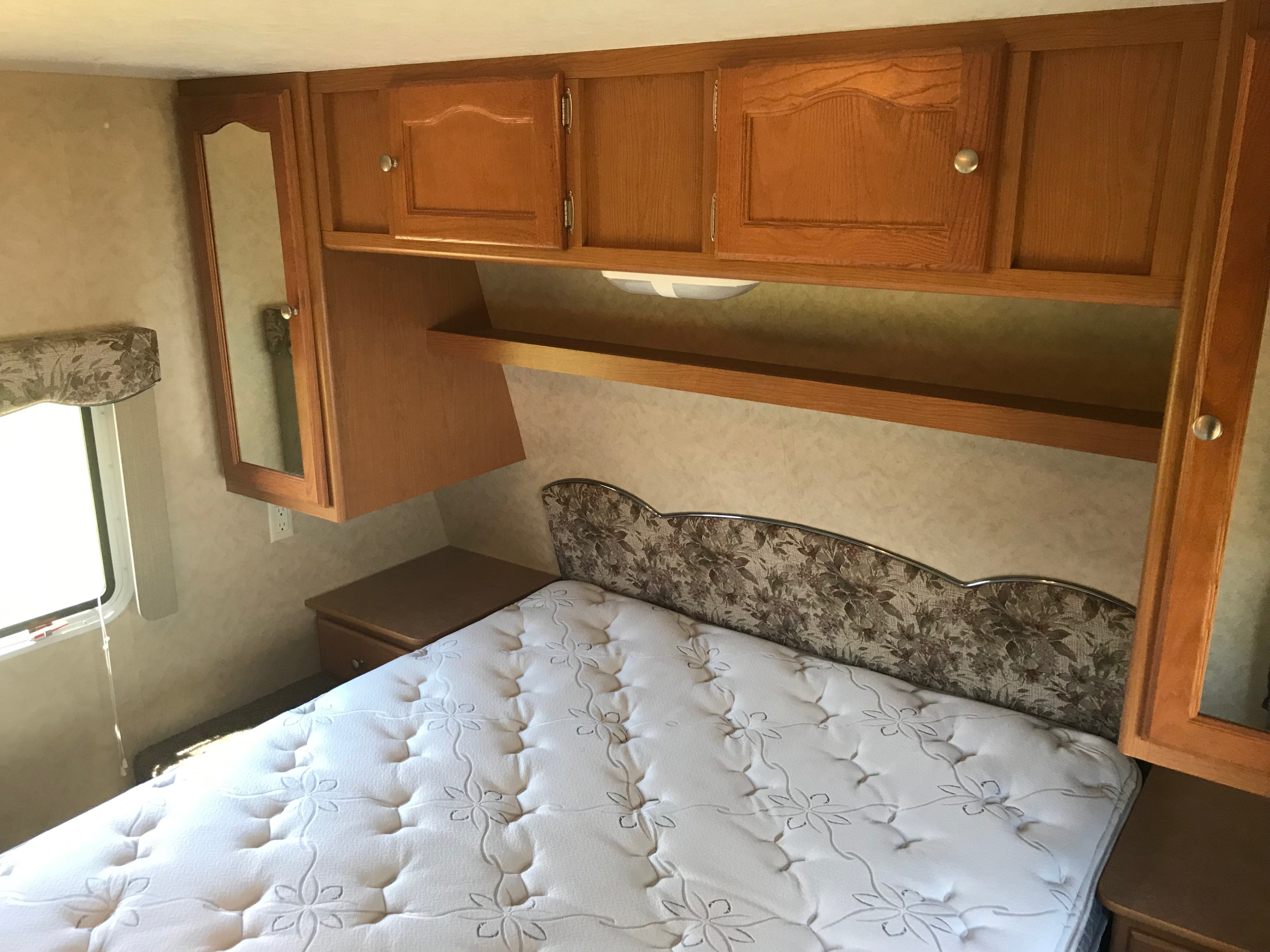 Cozy RV rental bedroom featuring a bed with patterned mattress, floral headboard, and wood cabinetry.. Dutchmen Dutchmen 2007