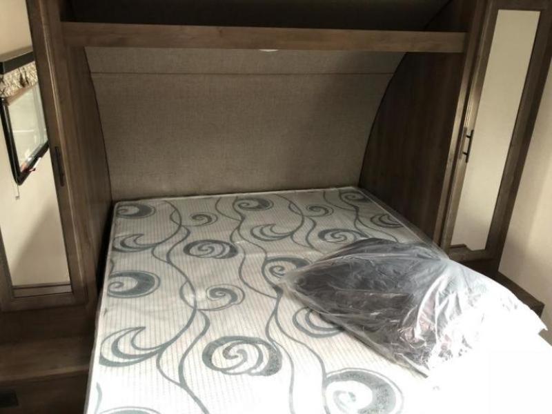 View of an RV rental bedroom featuring a patterned mattress, overhead storage, wall-mounted TV, and mirrored closet.. K-Z Manufacturing Other 2019