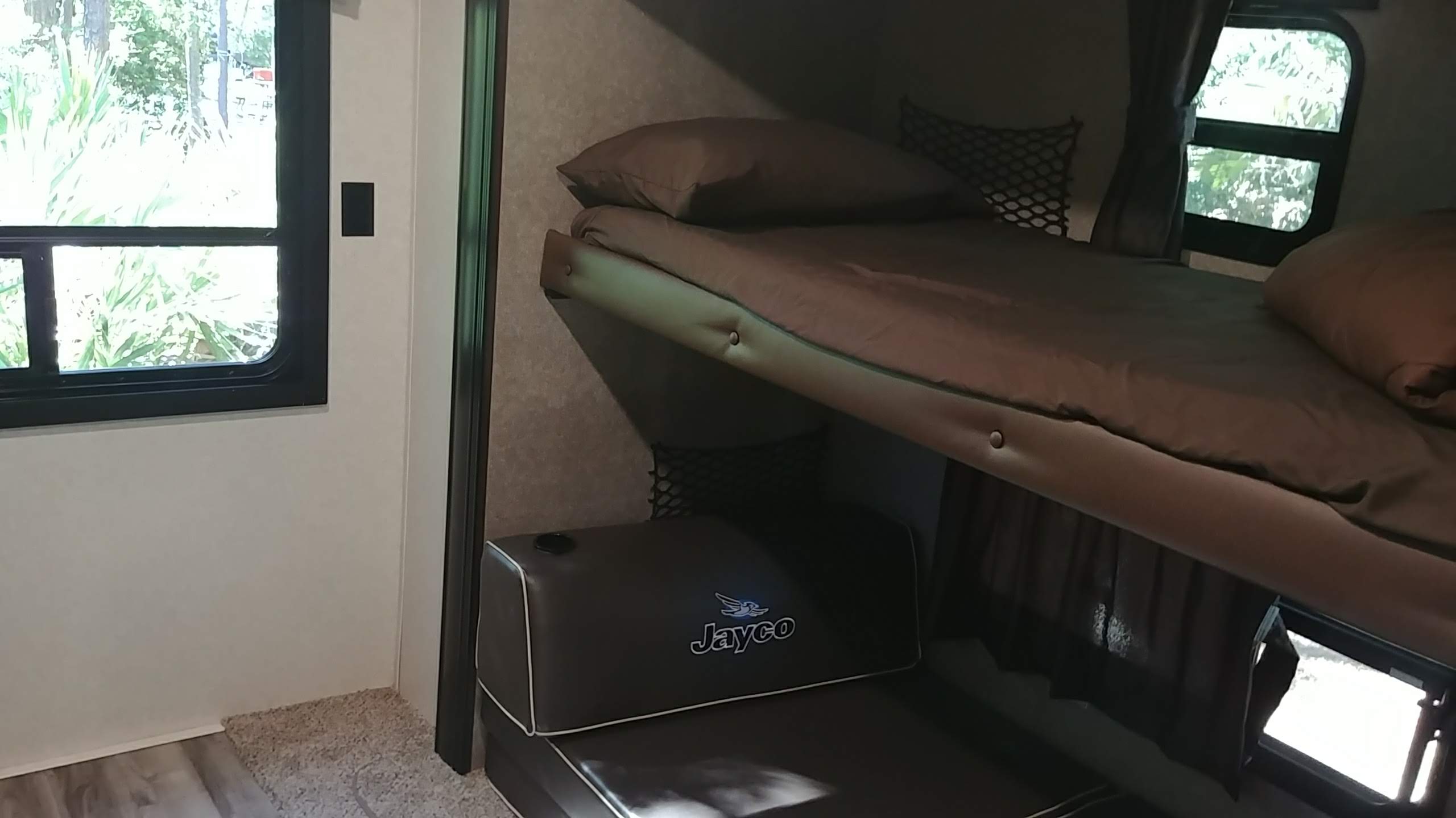 This RV rental features comfortable brown bunk beds, a lower Jayco branded cushion, and a window view to nature outside.. Jayco Jay Flight 2018