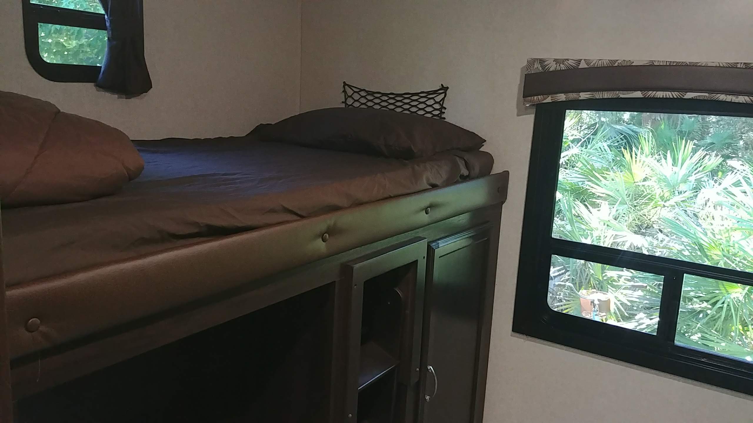 Cozy rv rental bunk bed area with brown bedding, safety net, lower storage, and windows revealing outdoor foliage.. Jayco Jay Flight 2018