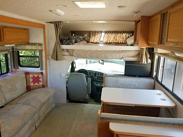 Spacious RV rental interior featuring a couch, dinette, kitchen cabinets, and bunk bed over the cab area.. Winnebago Minnie 2004