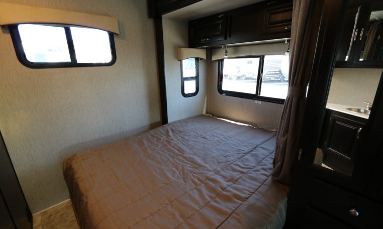 This RV rental offers a well-lit bedroom with a cozy bed, windows, and dark cabinetry, ideal for comfortable travel.. Nexus RV Phantom 2019