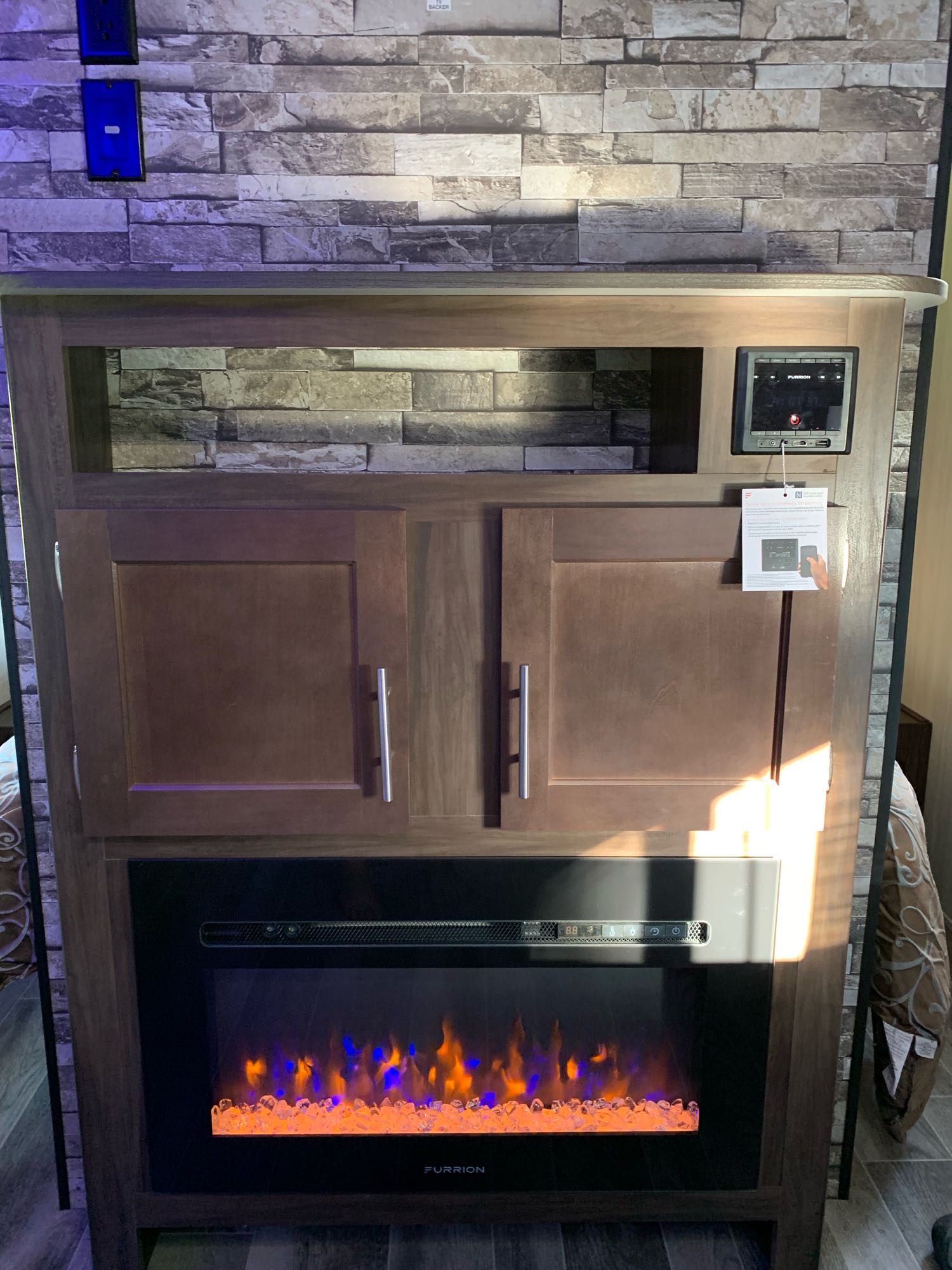 Inside an RV rental: functional entertainment center with a glowing electric fireplace below cabinets and controls.. Forest River Cherokee Grey Wolf 2020