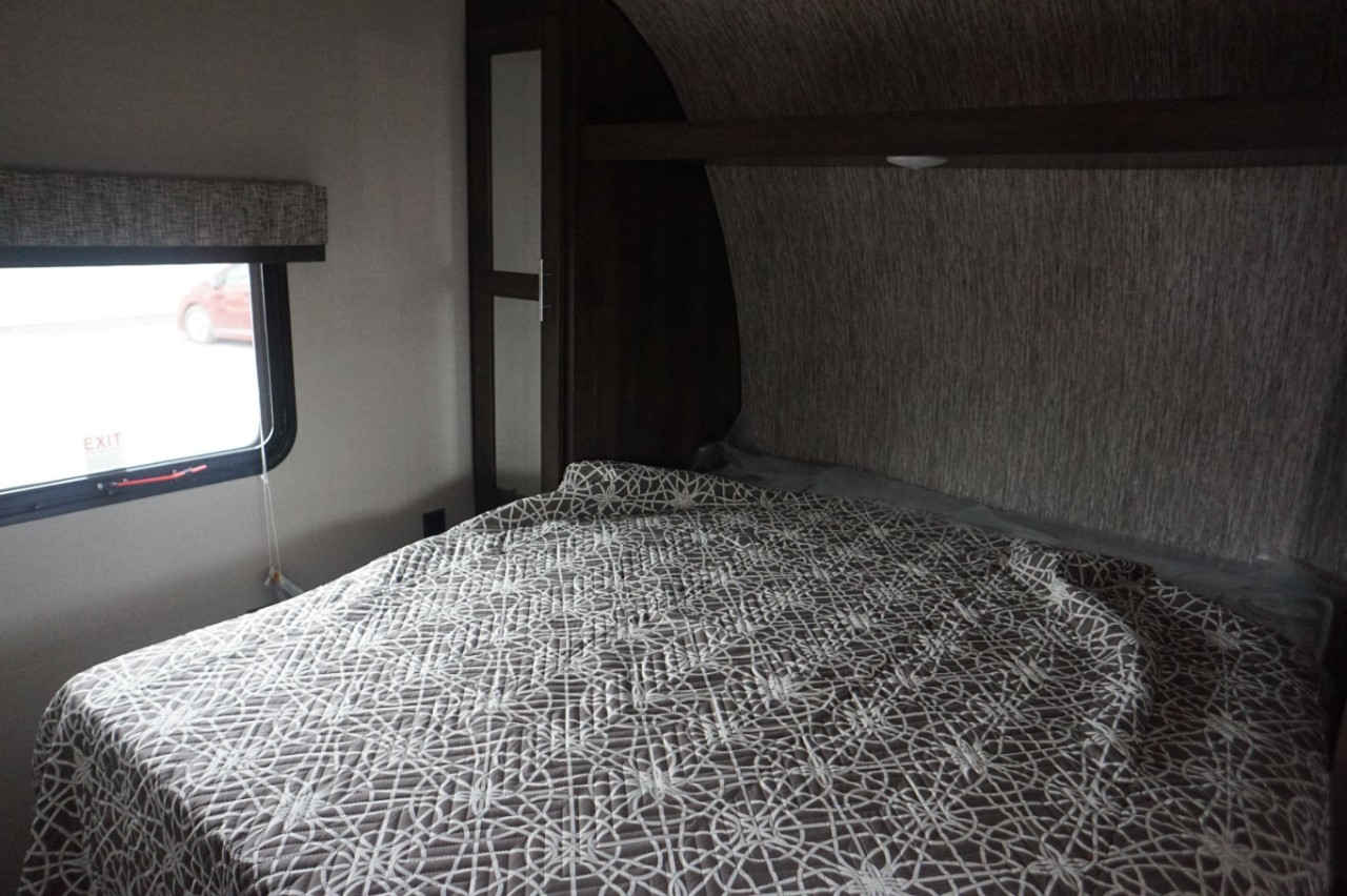 Comfortable RV rental bedroom with a patterned quilt, window with an EXIT sign, and built-in storage.. K-Z Manufacturing sportsmen 301bhse 2020