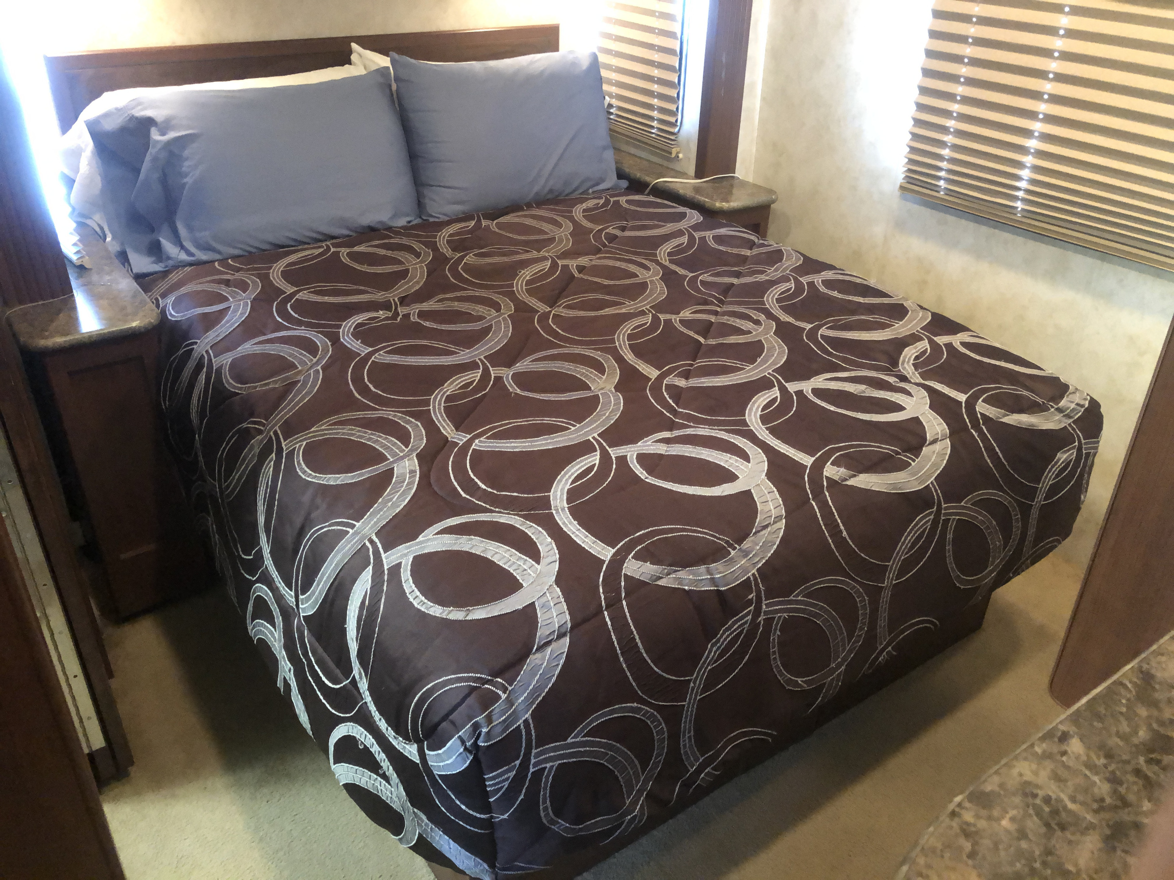 Comfortable bed in an RV rental, featuring a patterned comforter, blue pillows, and blinds for privacy.. Tioga Tioga Motorhome 2011