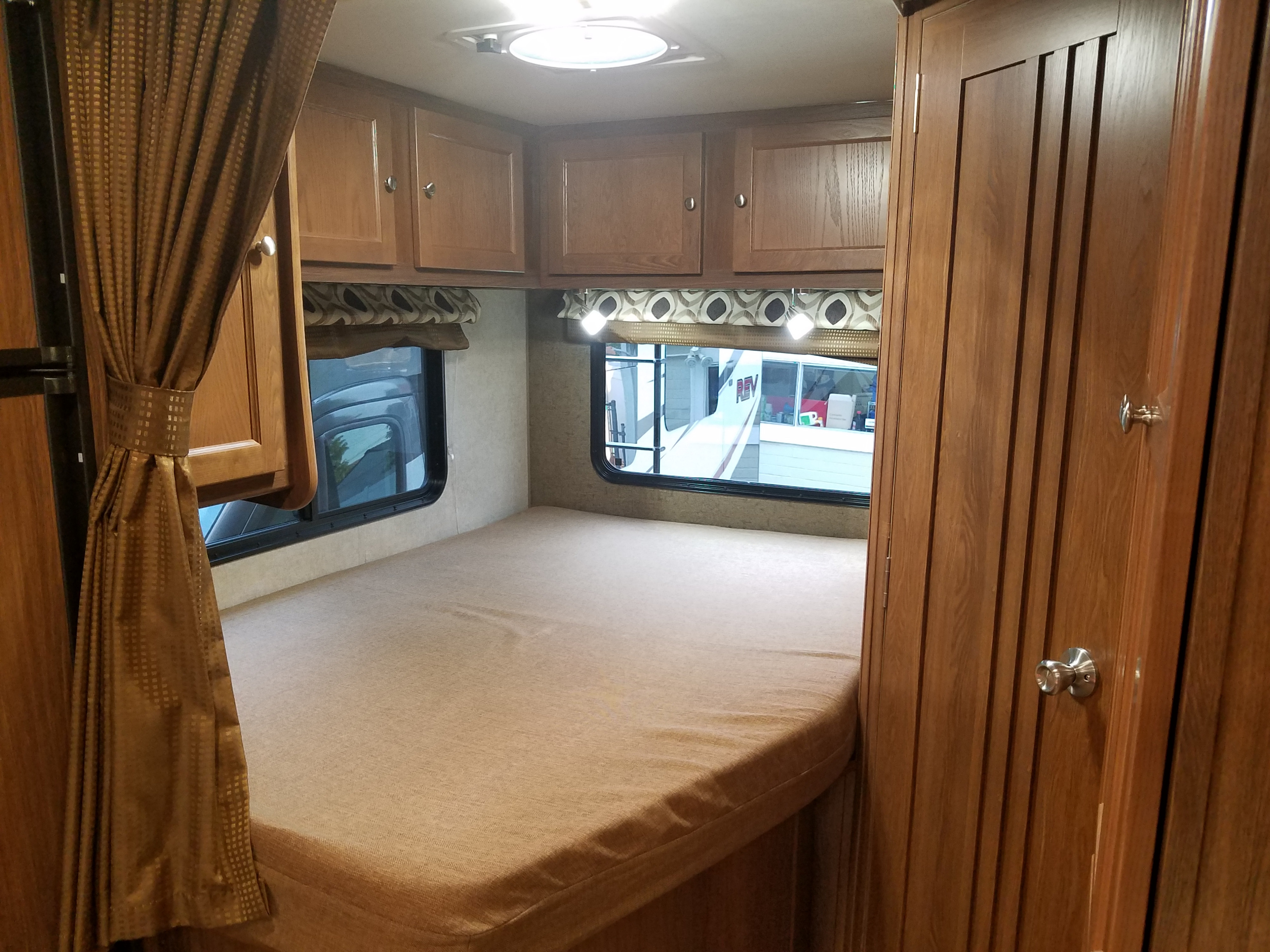 Inside a cozy RV rental: a compact bedroom featuring a comfortable bed, wood cabinets, and two large windows.. Forest River Coachmen Leprechaun 2017