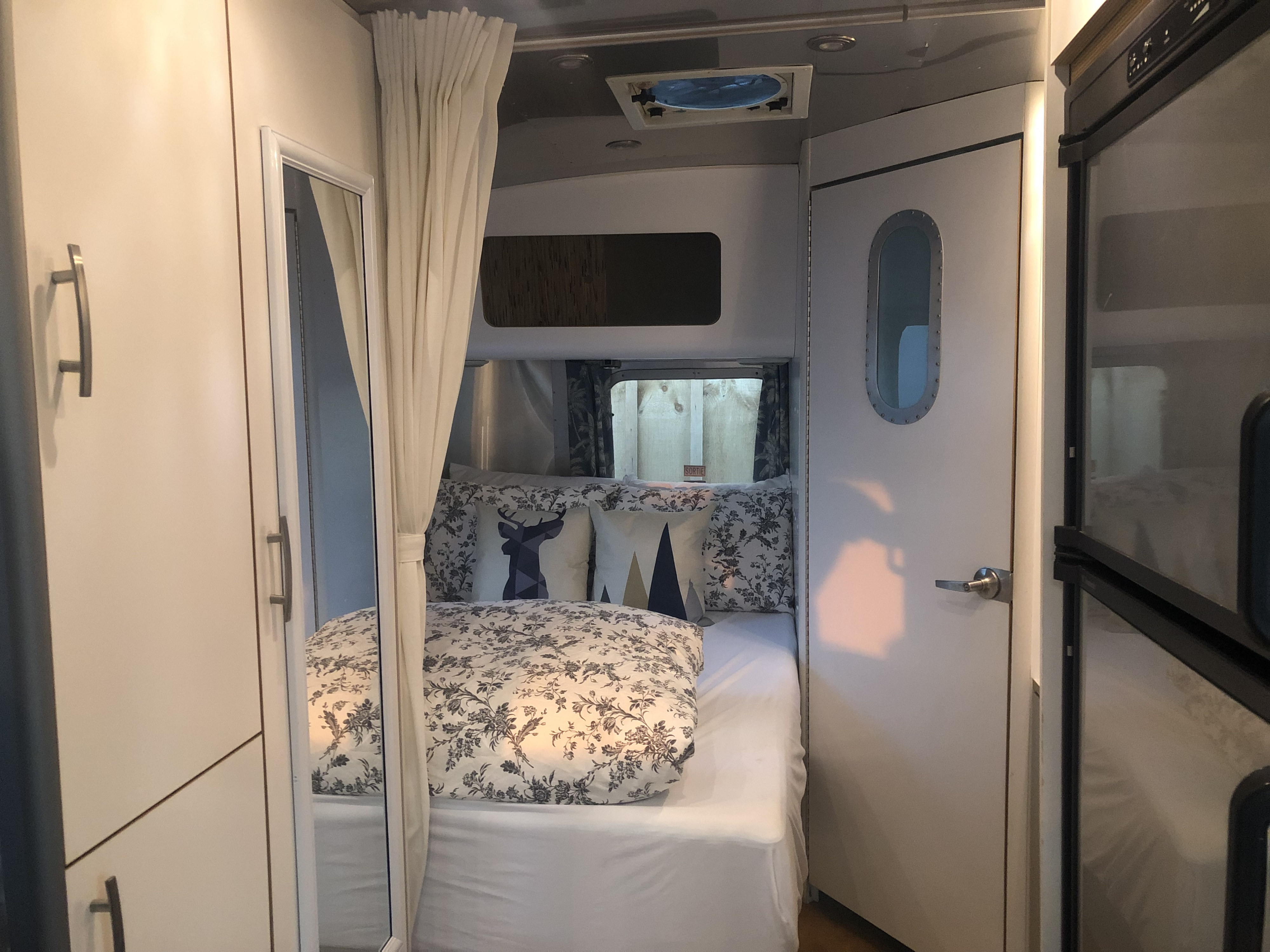 Cozy RV rental bedroom with patterned bedding, a mirrored cabinet, and a porthole door leading to more living space.. Airstream International 2007
