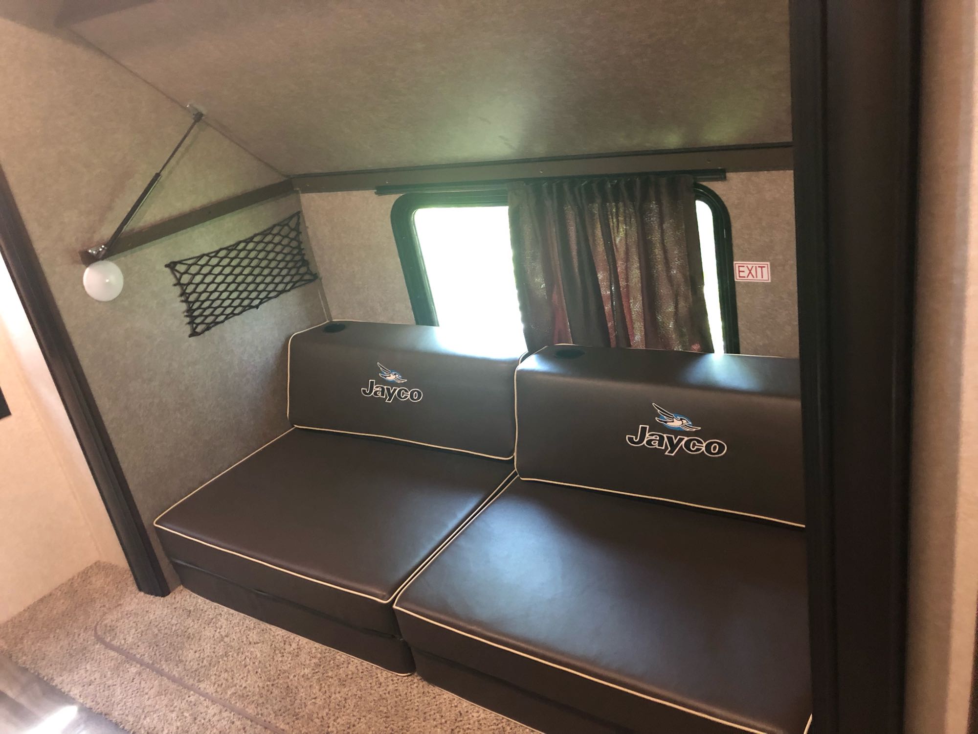 RV rental interior with dark Jayco seating, side window, EXIT sign, and wall storage. A cozy space for your travels.. Jayco Other 2020