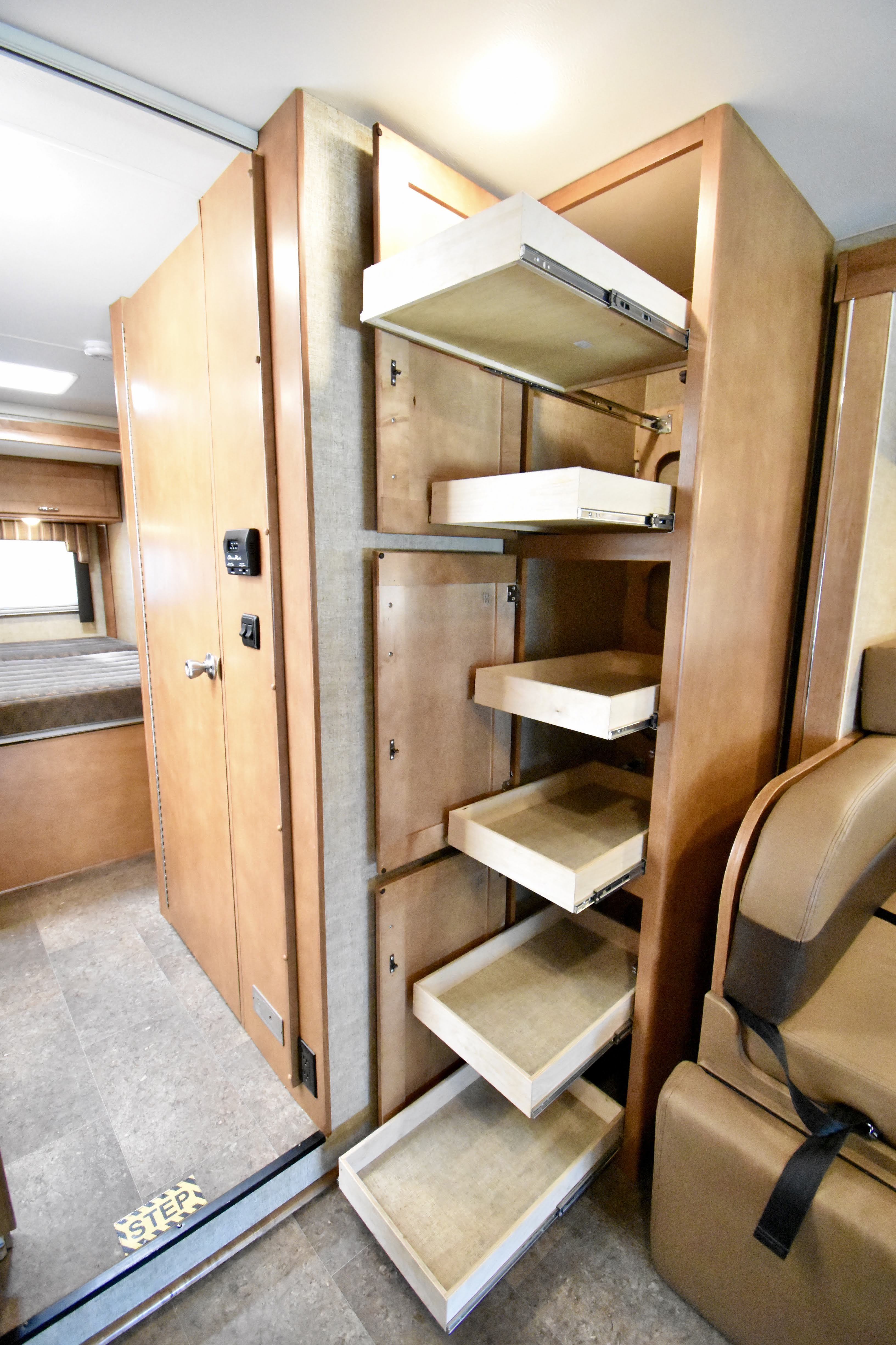 RV rental interior: A multi-tiered cabinet with deep, pull-out pantry shelves, beside a bedroom entrance.. Winnebago Minnie Winnie 2018