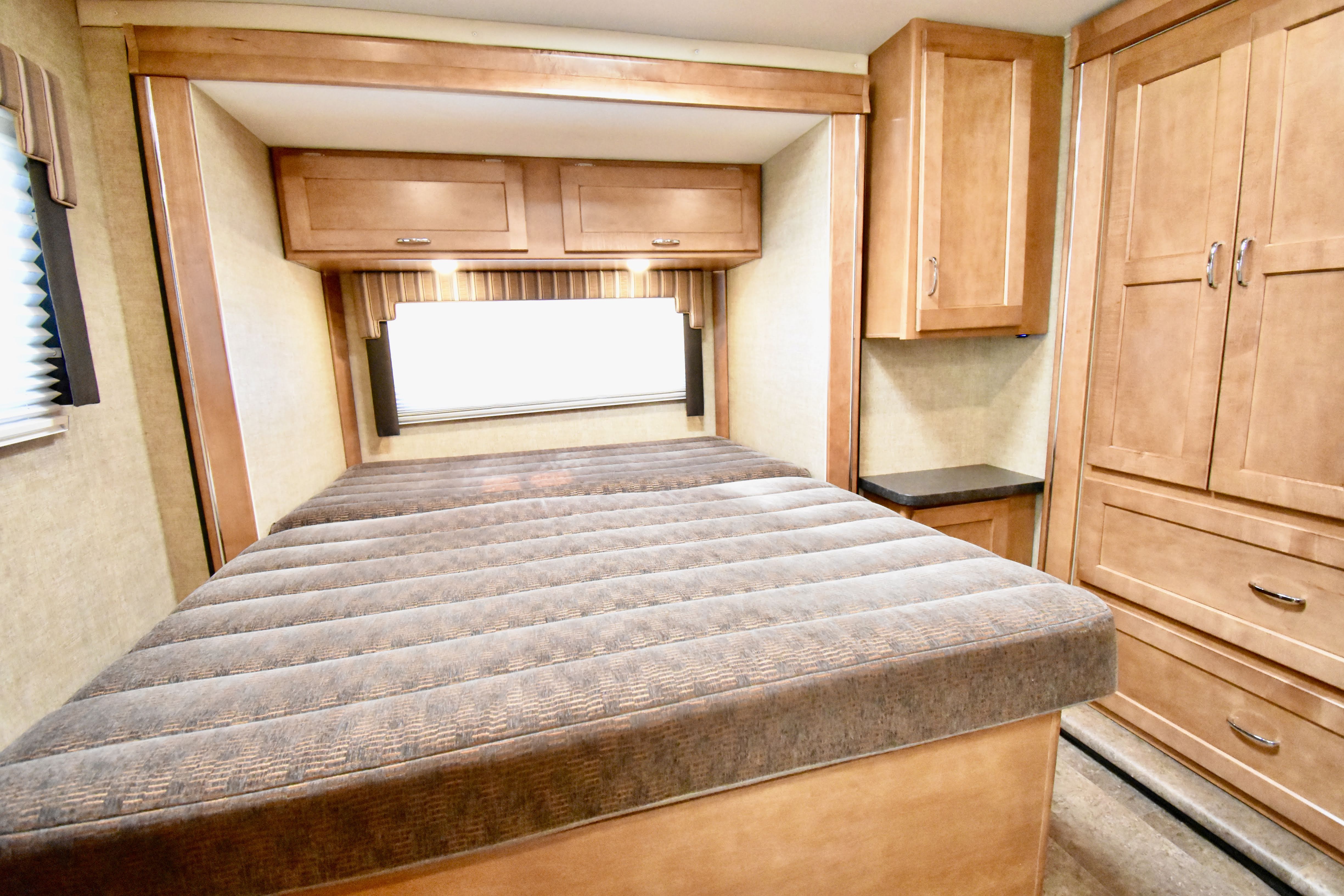 Explore this compact RV rental bedroom featuring a striped bed, wood cabinets, and ample storage.. Winnebago Minnie Winnie 2018