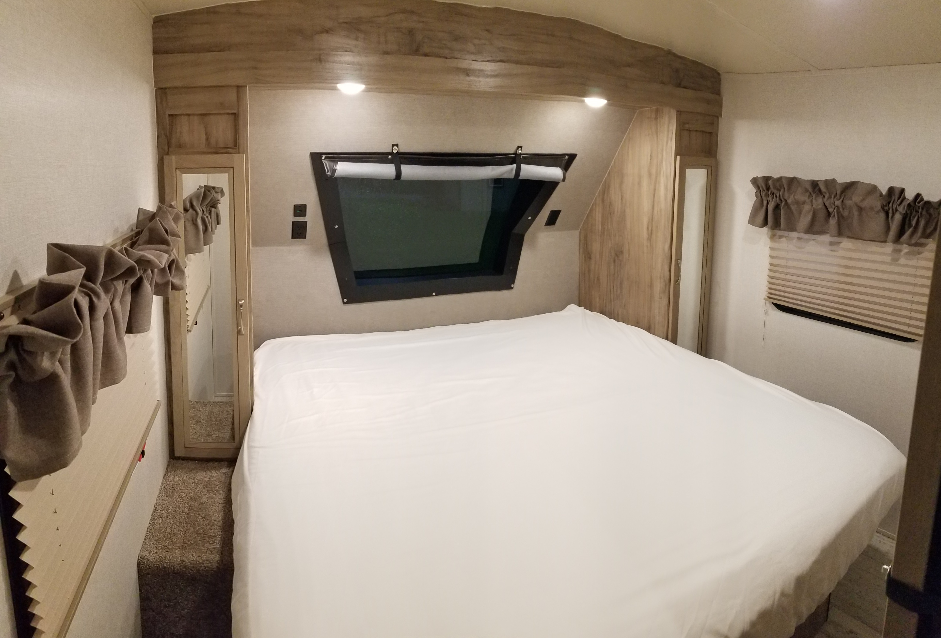 Clean RV rental bedroom features a large bed with white sheets, window, and wood accents.. Palomino Solaire Ultra Lite 268BHSK 2020
