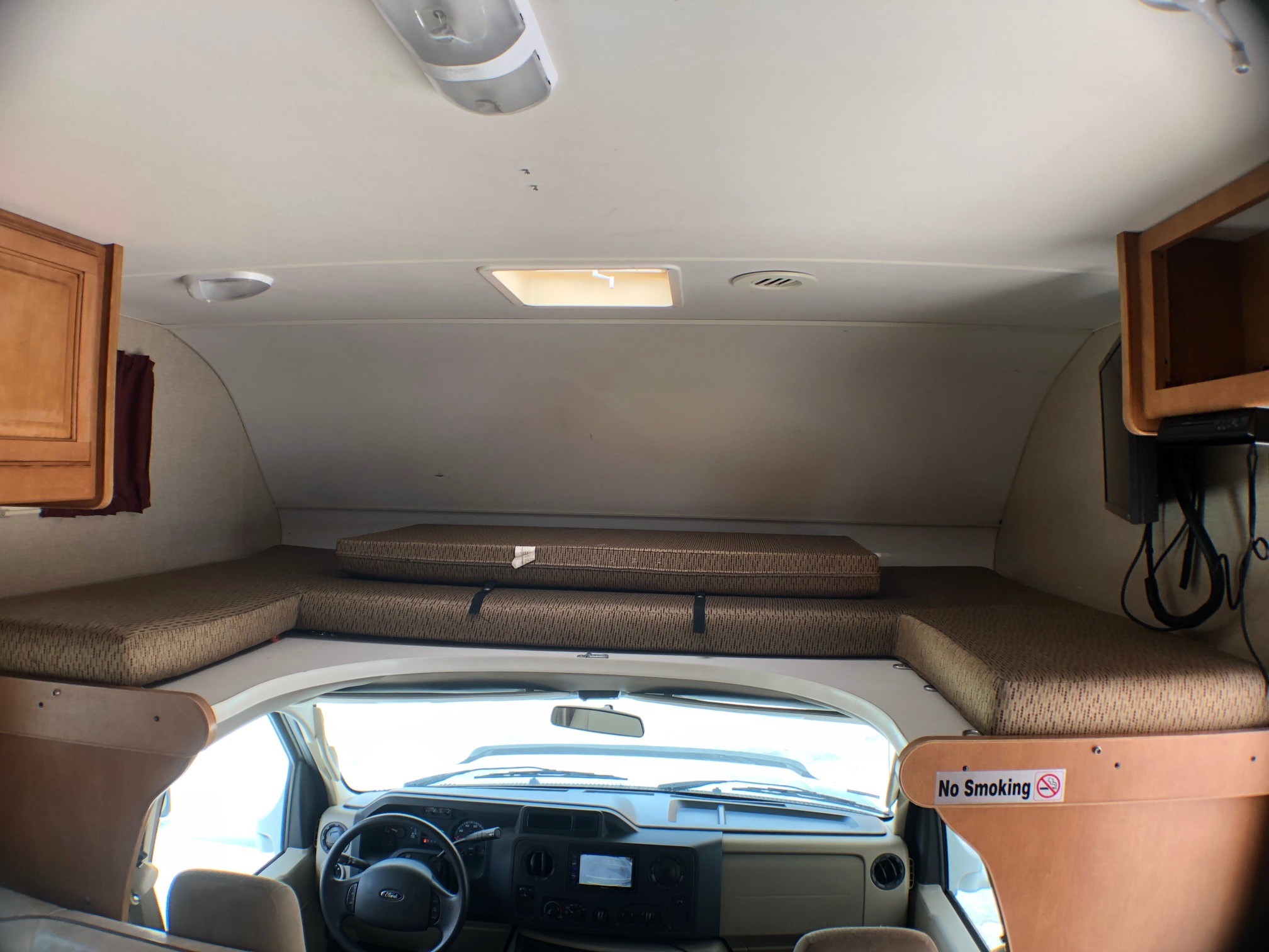 Interior of an RV rental, showing the driver's cabin and an overhead sleeping bunk with mattresses, lights, and a skylight.. Winnebago Minnie Winnie 2016