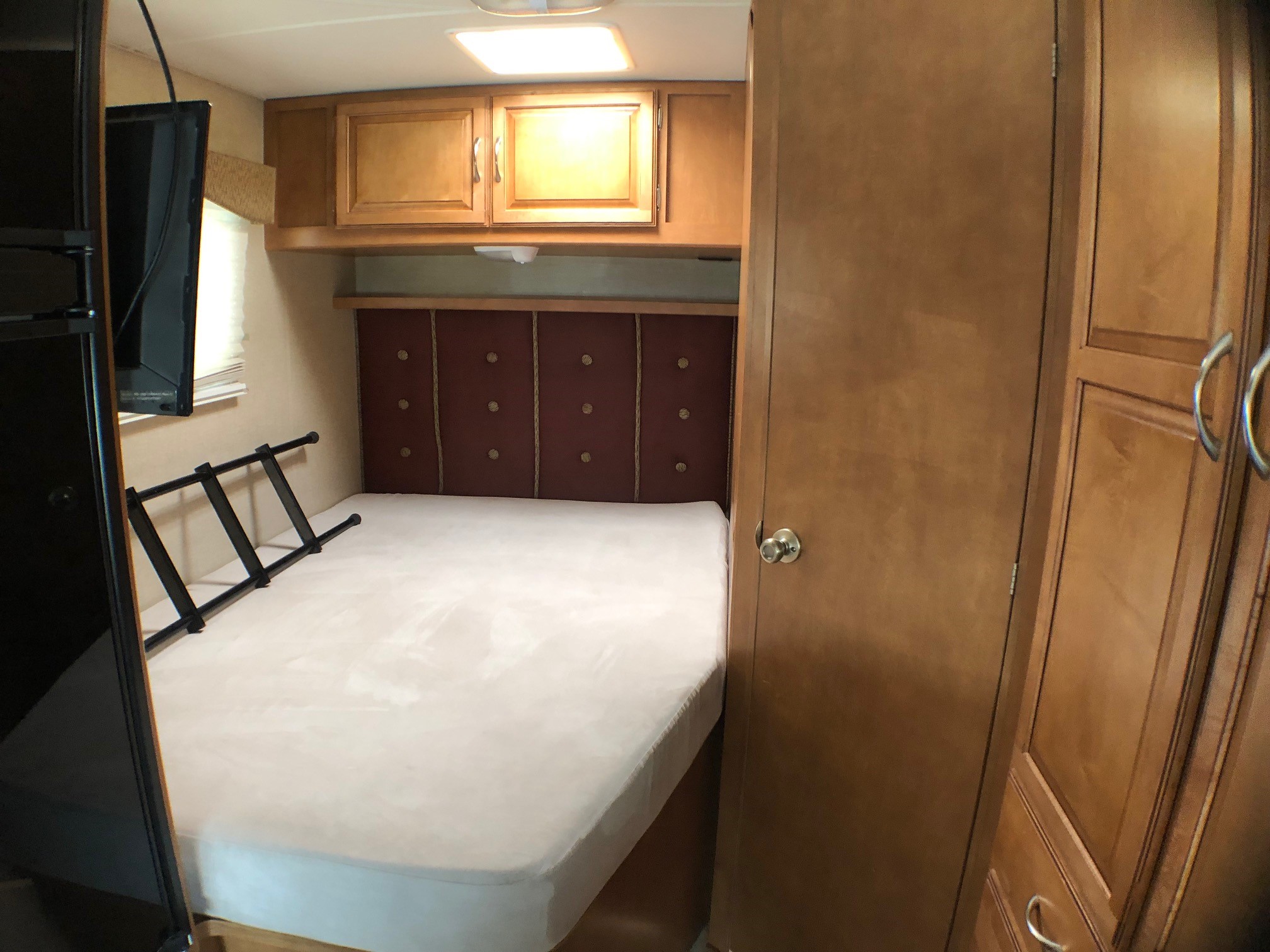 Cozy RV rental bedroom featuring a bed, red upholstered headboard, and wood cabinetry with a TV. Ready for your trip.. Winnebago Minnie Winnie 2016
