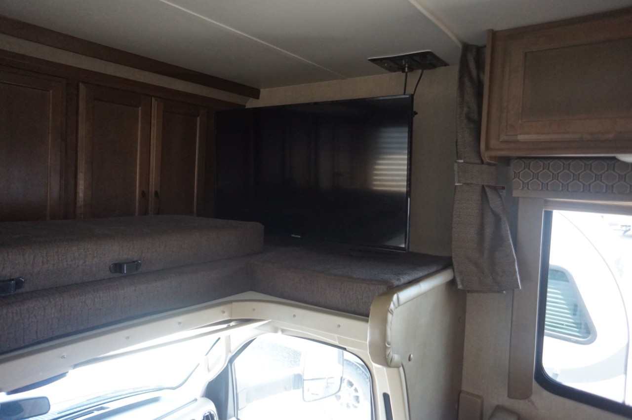 View inside an RV rental of the cab-over bunk, a large TV, wood cabinets, and window.. Gulf Stream conquest 2020