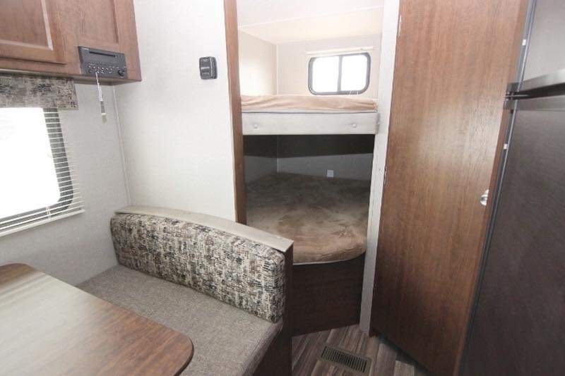 RV rental interior: A compact living space featuring a cozy dinette with a patterned bench and a dedicated bunk bed sleeping area.. Keystone Hideout 2018
